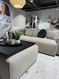  Helles beiges Sofa der Marke Roomio mit passendem Hocker; auf dem Hocker befindet sich eine abnehmbare Ablagefläche für Dekoration und Accessoires.