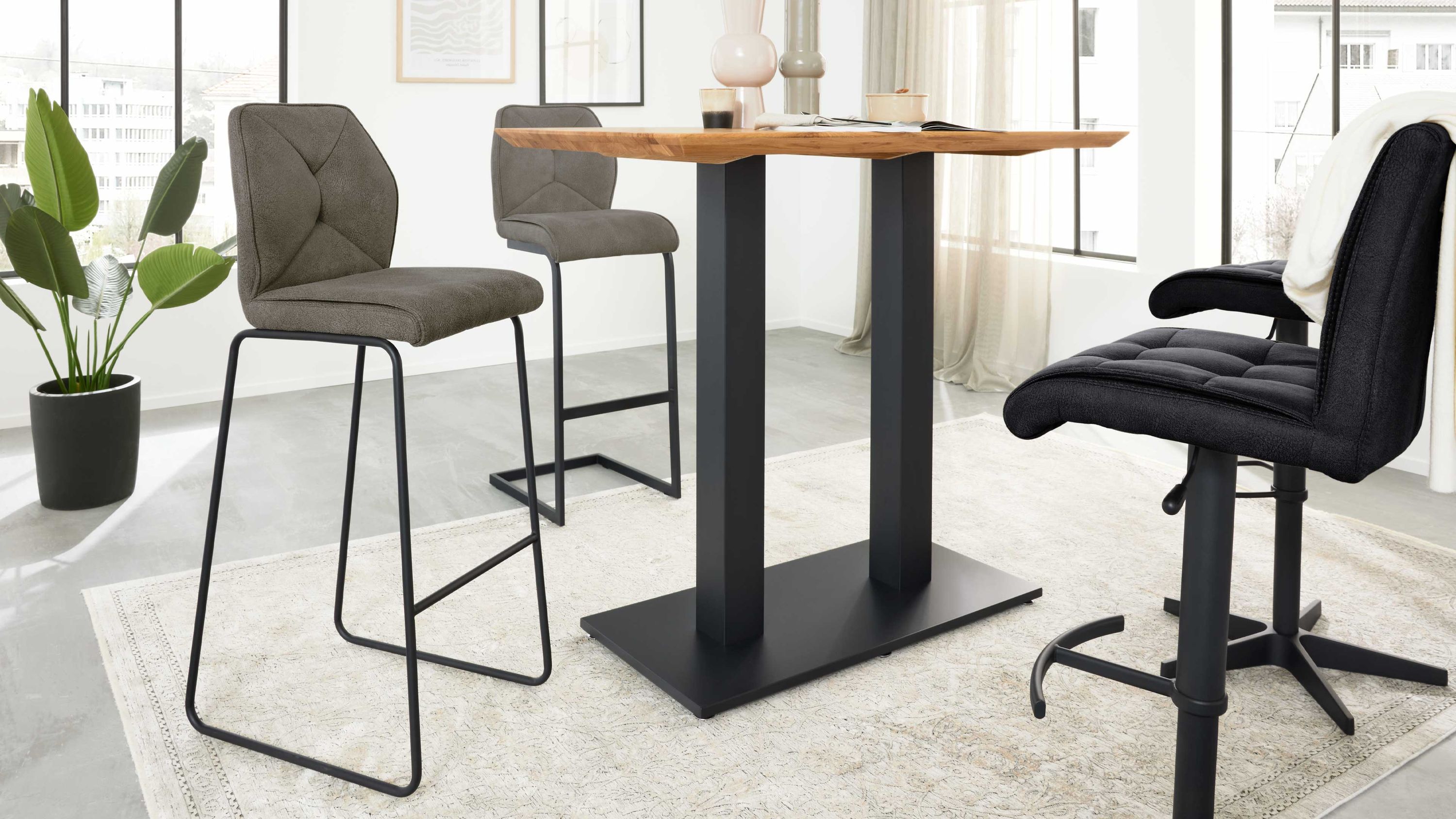 Dunkelgraue Barhocker mit gepolstertem Sitz und Rückenlehne schwarzes Metallgestell neben einem hohen Tisch