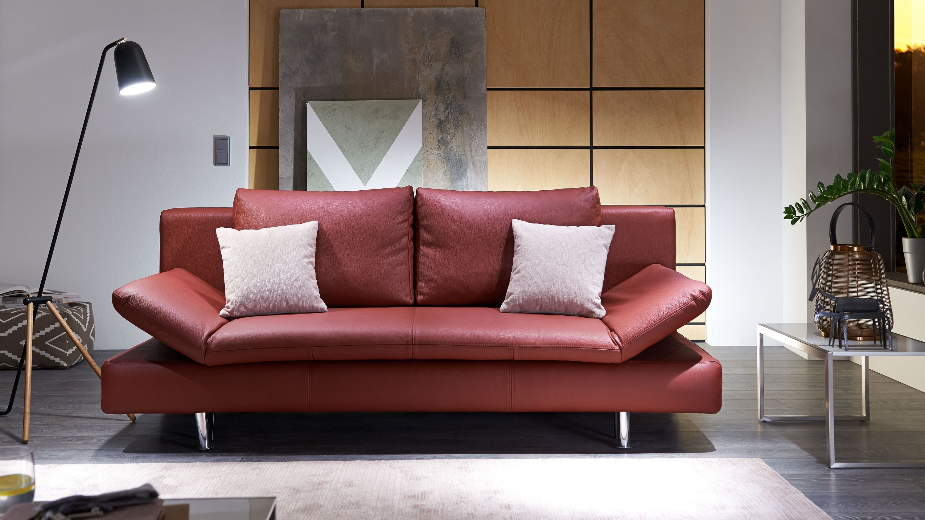 Schlafsofa in weinrot mit verchromten Metallfüßen und zwei hellen Kissen in modernem Wohnzimmer