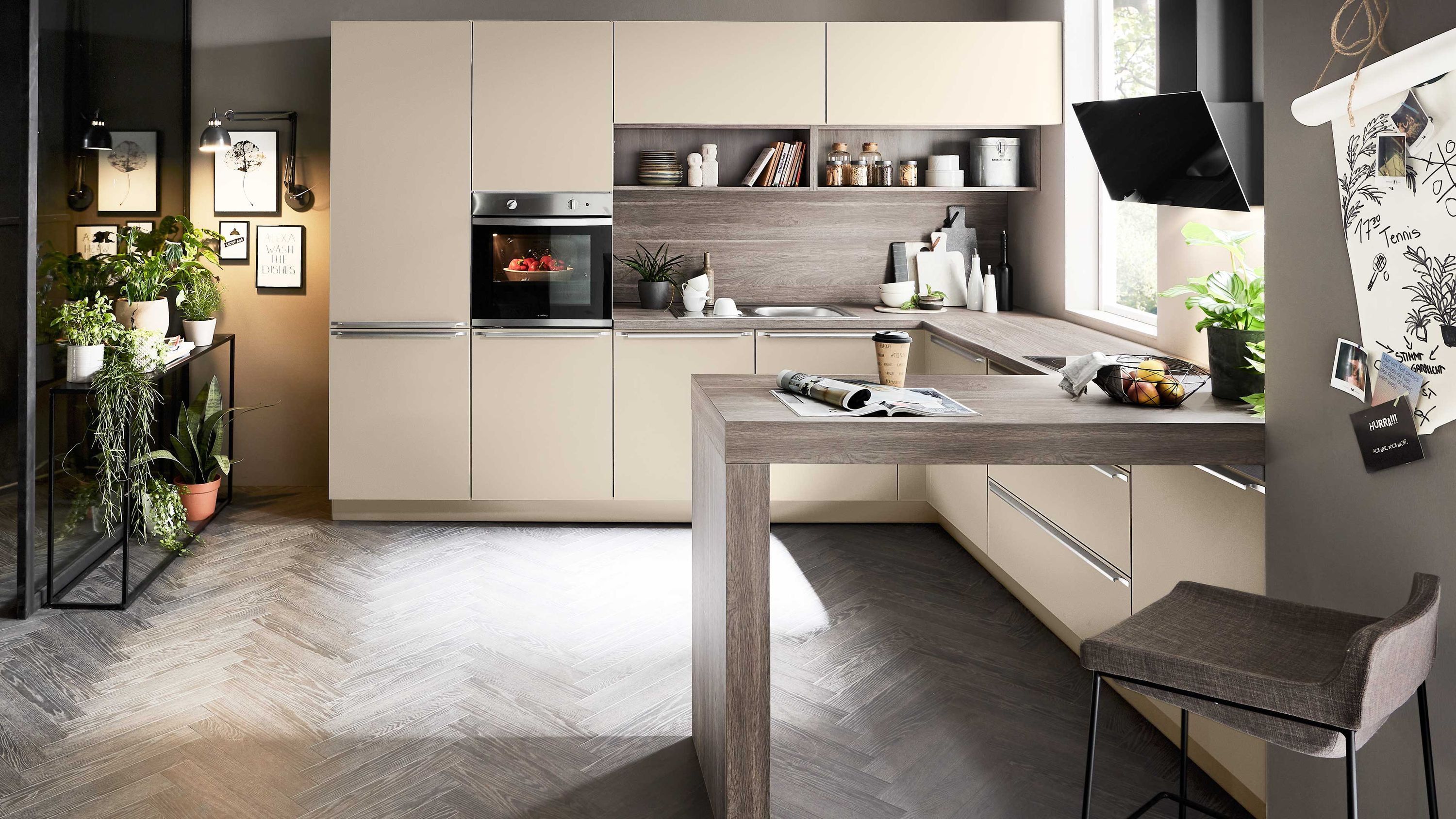 Moderne Küche mit Naturtönen funktionalem Design und wohnlichem Flair Beige Küche mit Holzinsel Herringbone-Boden Einbauofen Pflanzen Wandmonitor offene Regale mit Gläsern