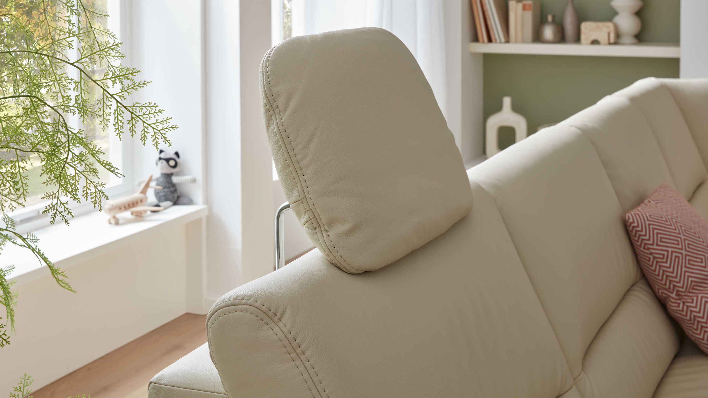 Beige Kopfstütze an einem hellen Sofa in einem Wohnzimmer mit Fenster und Regal