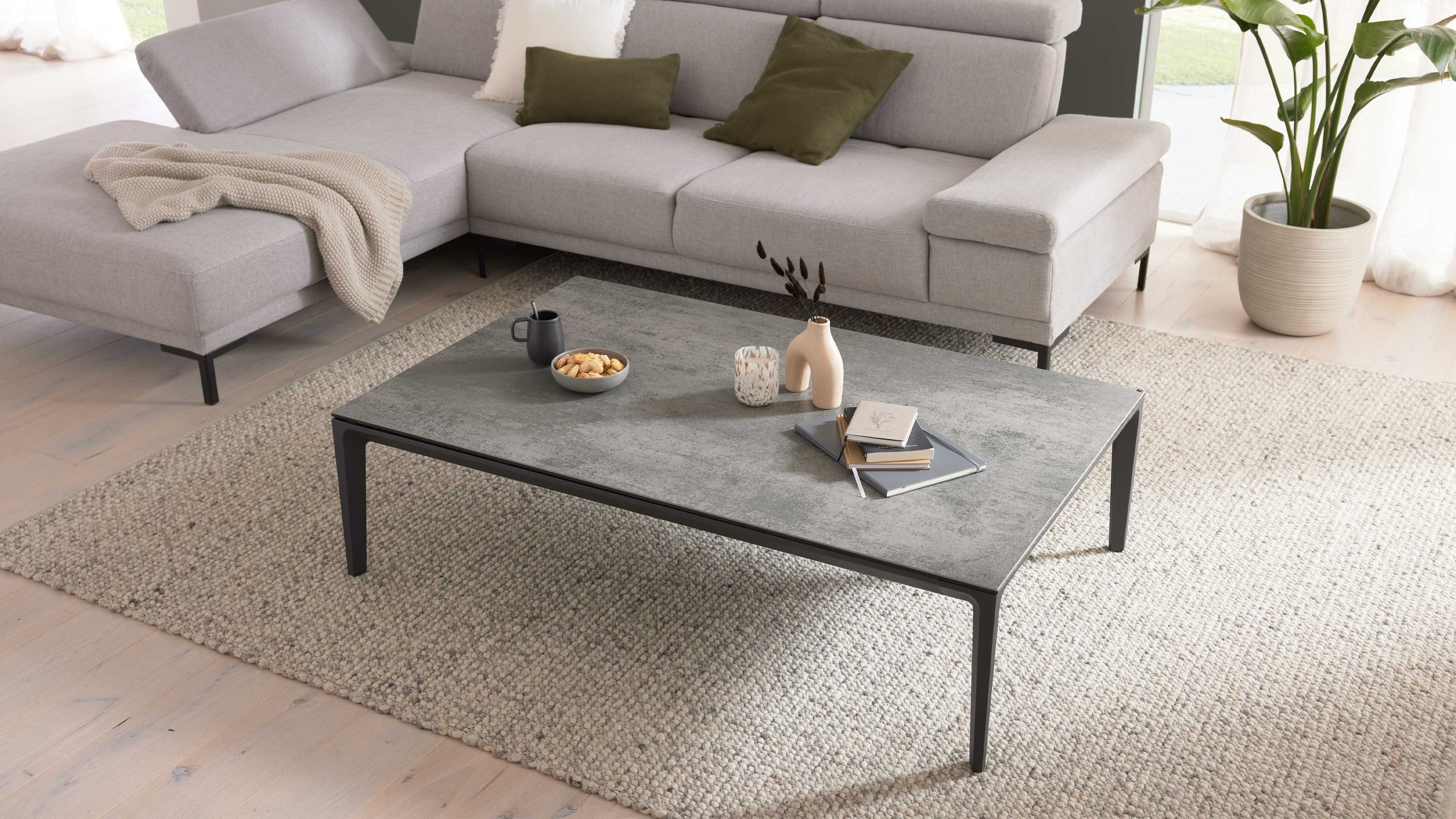 Rechteckiger Couchtisch mit silbergrauer Oberfläche und schwarzem Gestell auf hellem Teppich vor grauem Sofa