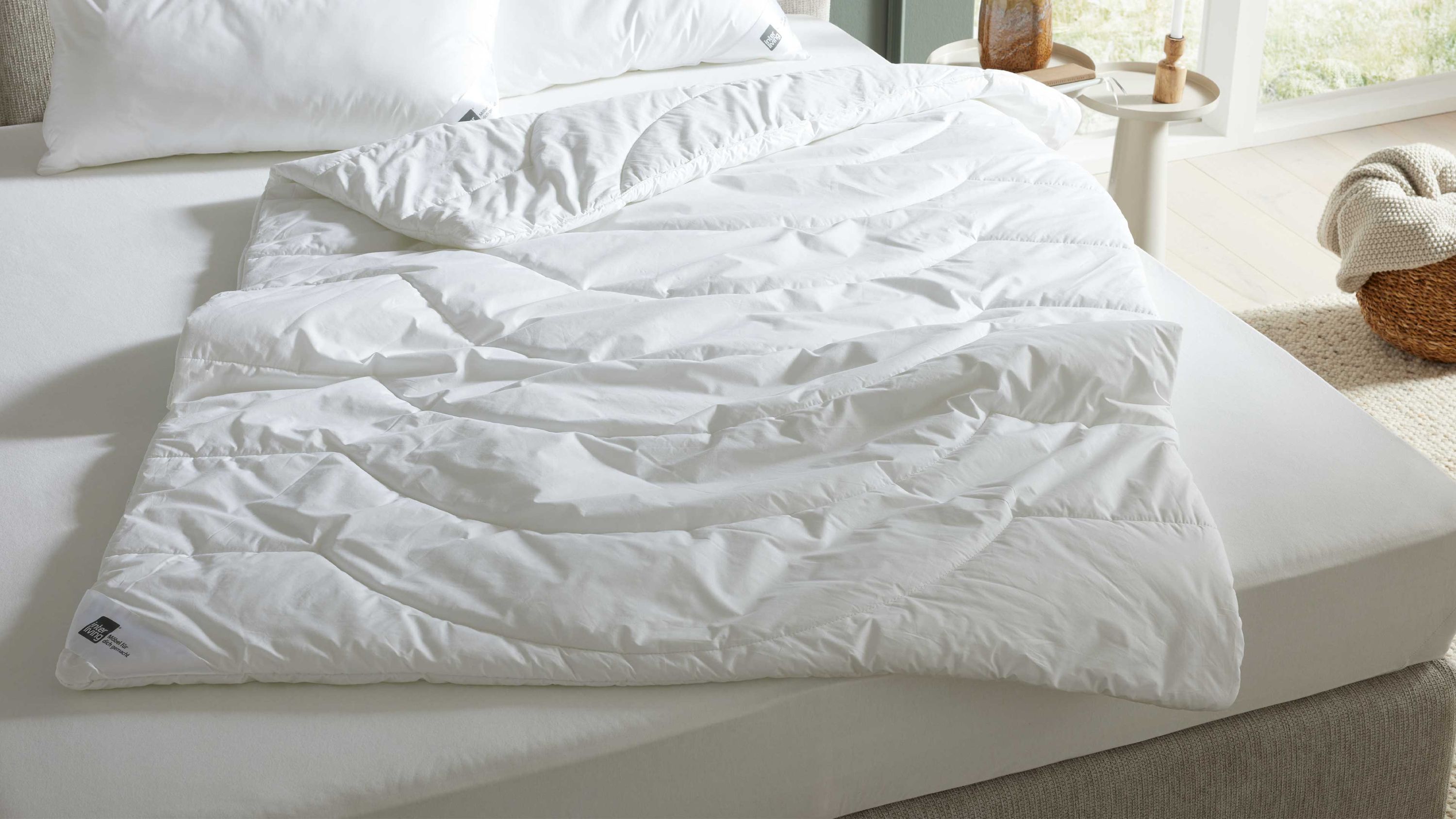 Weiße Bettdecke mit Steppmuster auf einem hellen Bett liegend