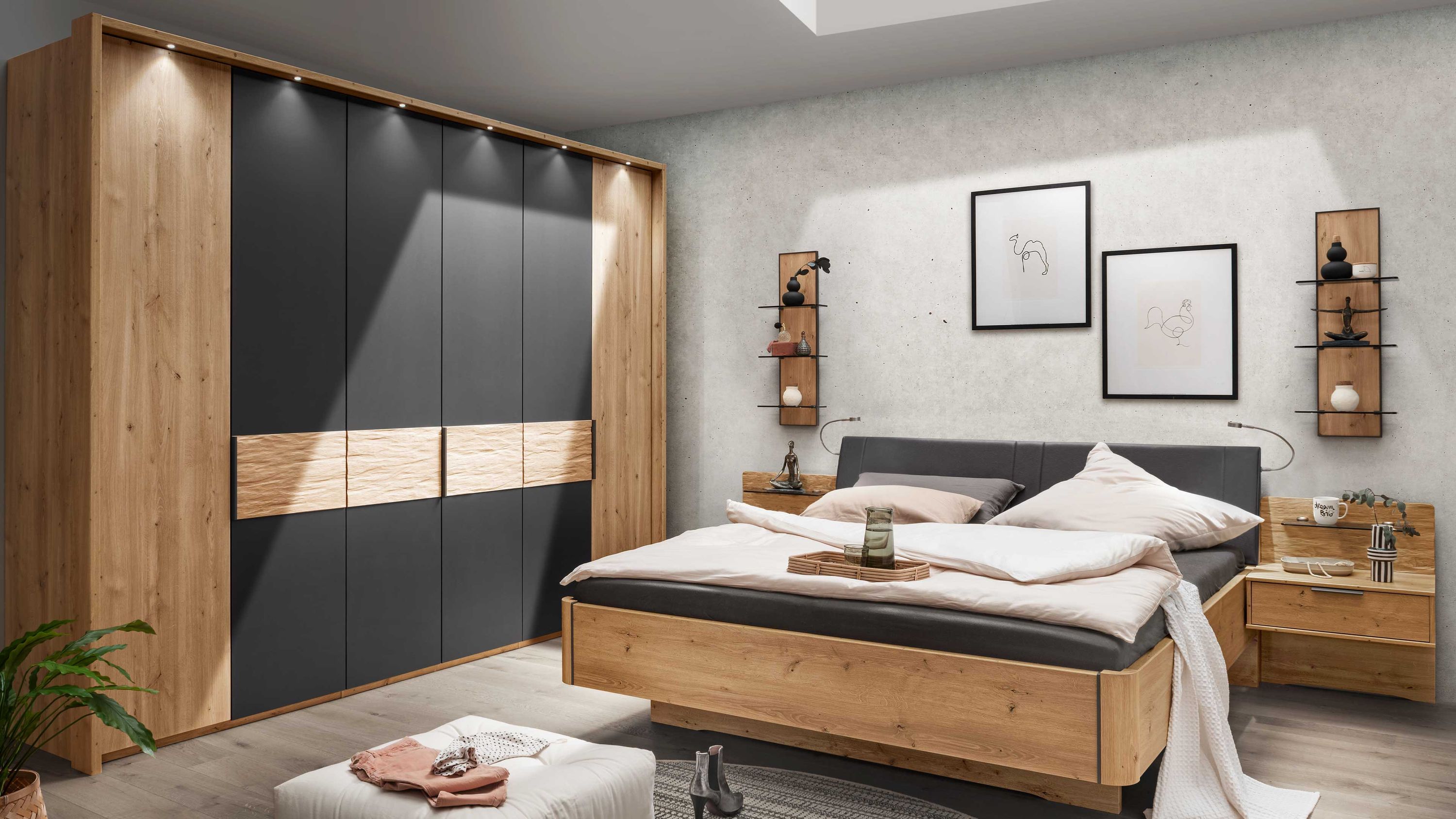 Schlafzimmer mit Bett in Holzoptik und dunklem Polsterkopfteil zwei Nachttischen und Hocker vor grauer Wand mit Bildern