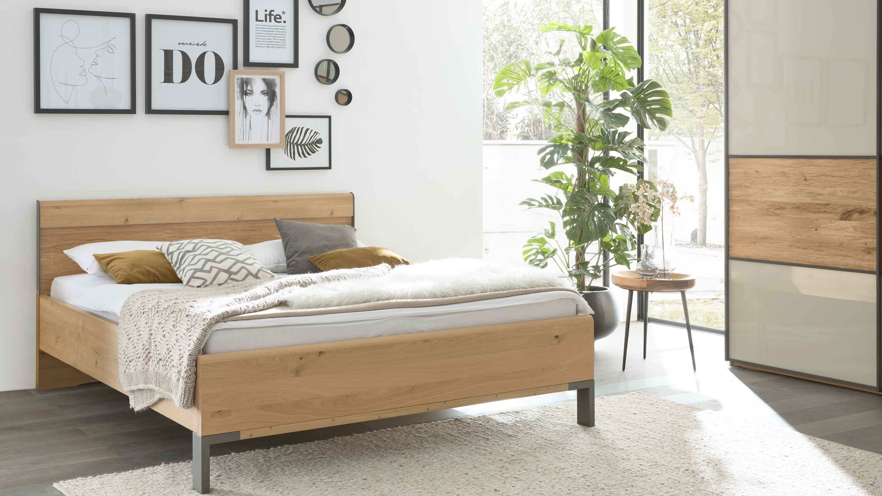 Bettgestell aus hellem Holz mit Kopfteil und Fußteil graue Metallfüße im modernen Schlafzimmer mit Teppich und Pflanzen
