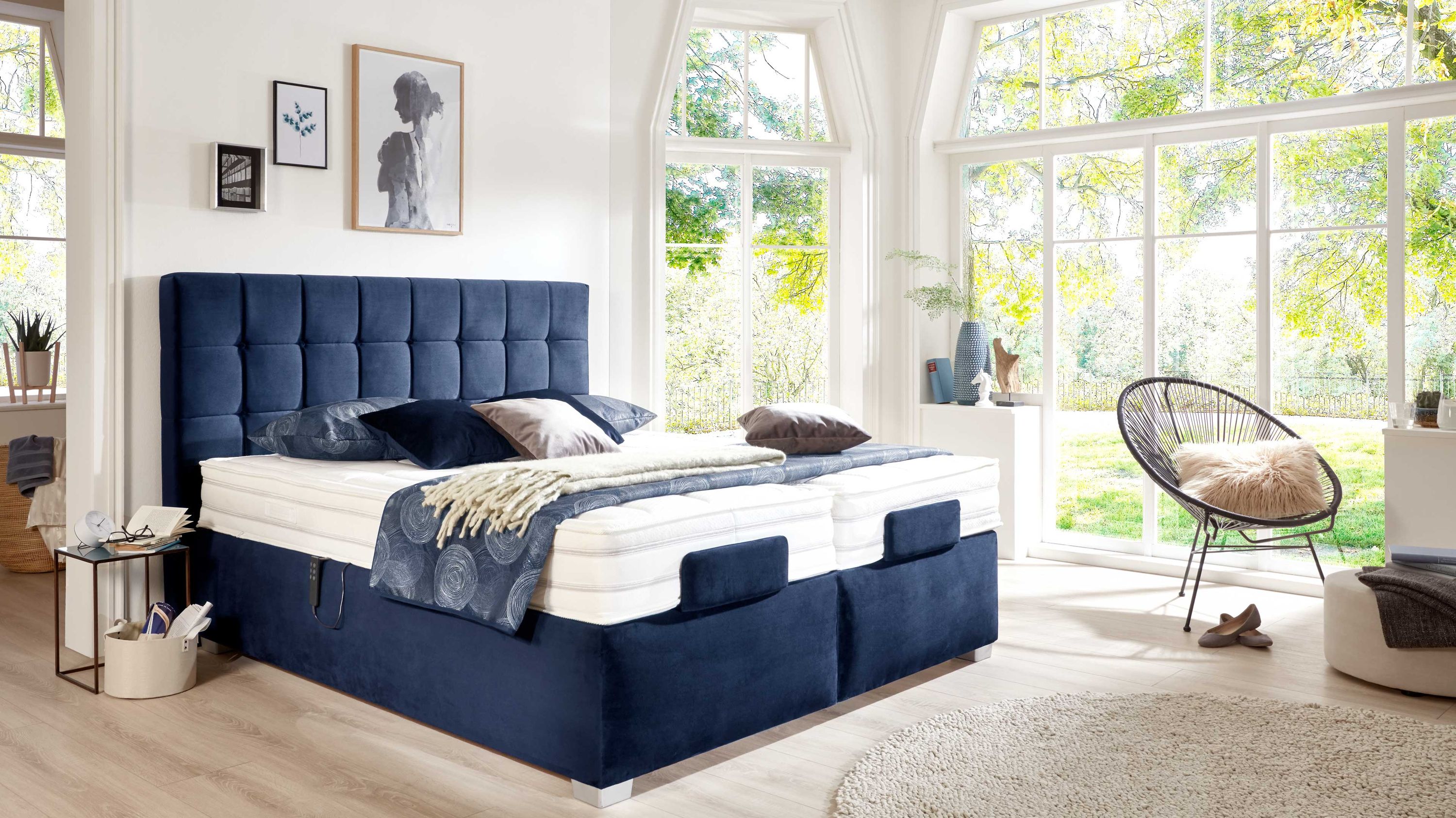 Boxspringbett mit gepolstertem dunkelblauem Kopfteil und weißer Matratze in hellem Schlafzimmer