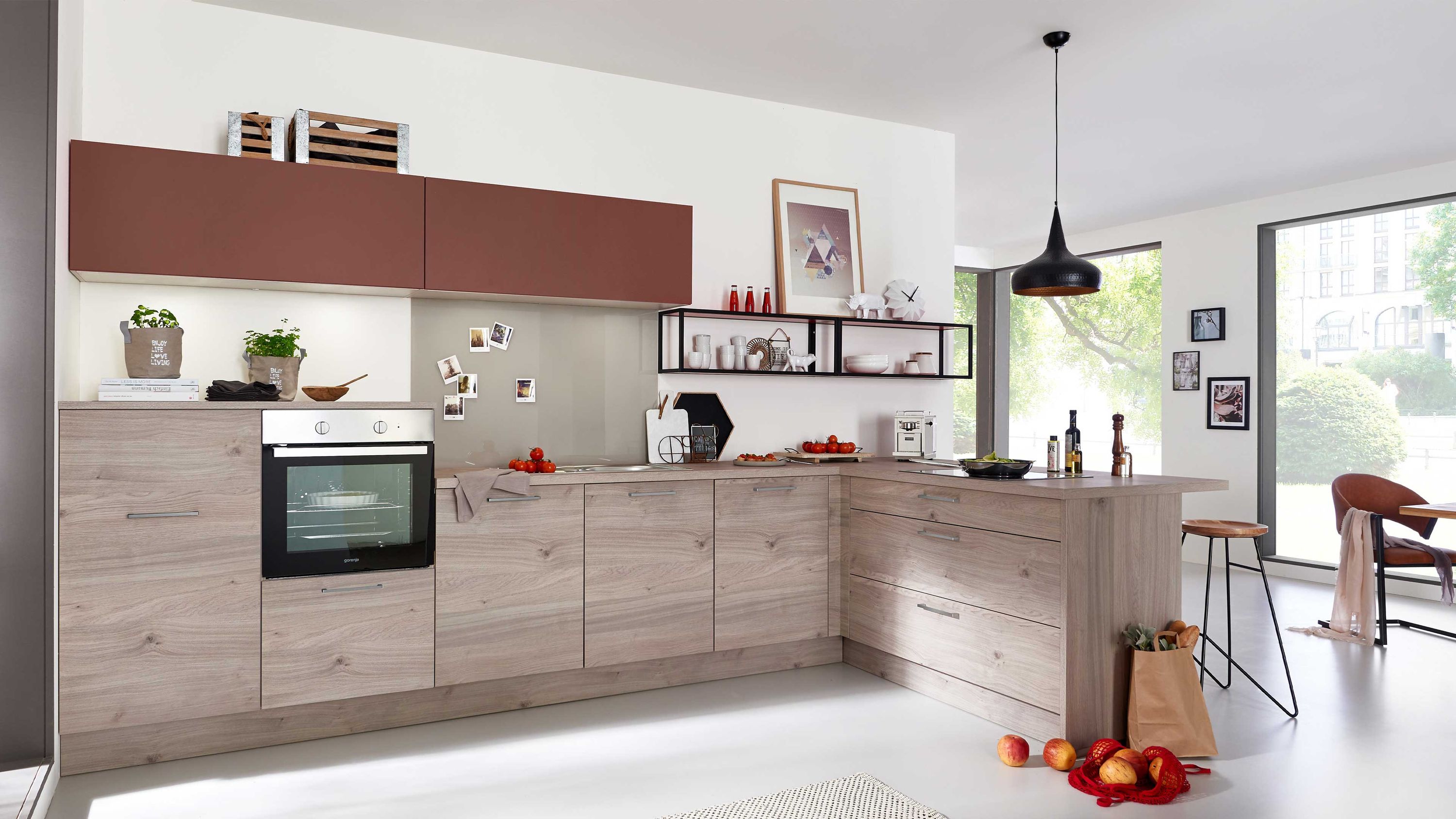 Küche mit Holzschränken Einbauofen roten Äpfeln großen Fenstern Esstisch im Hintergrund