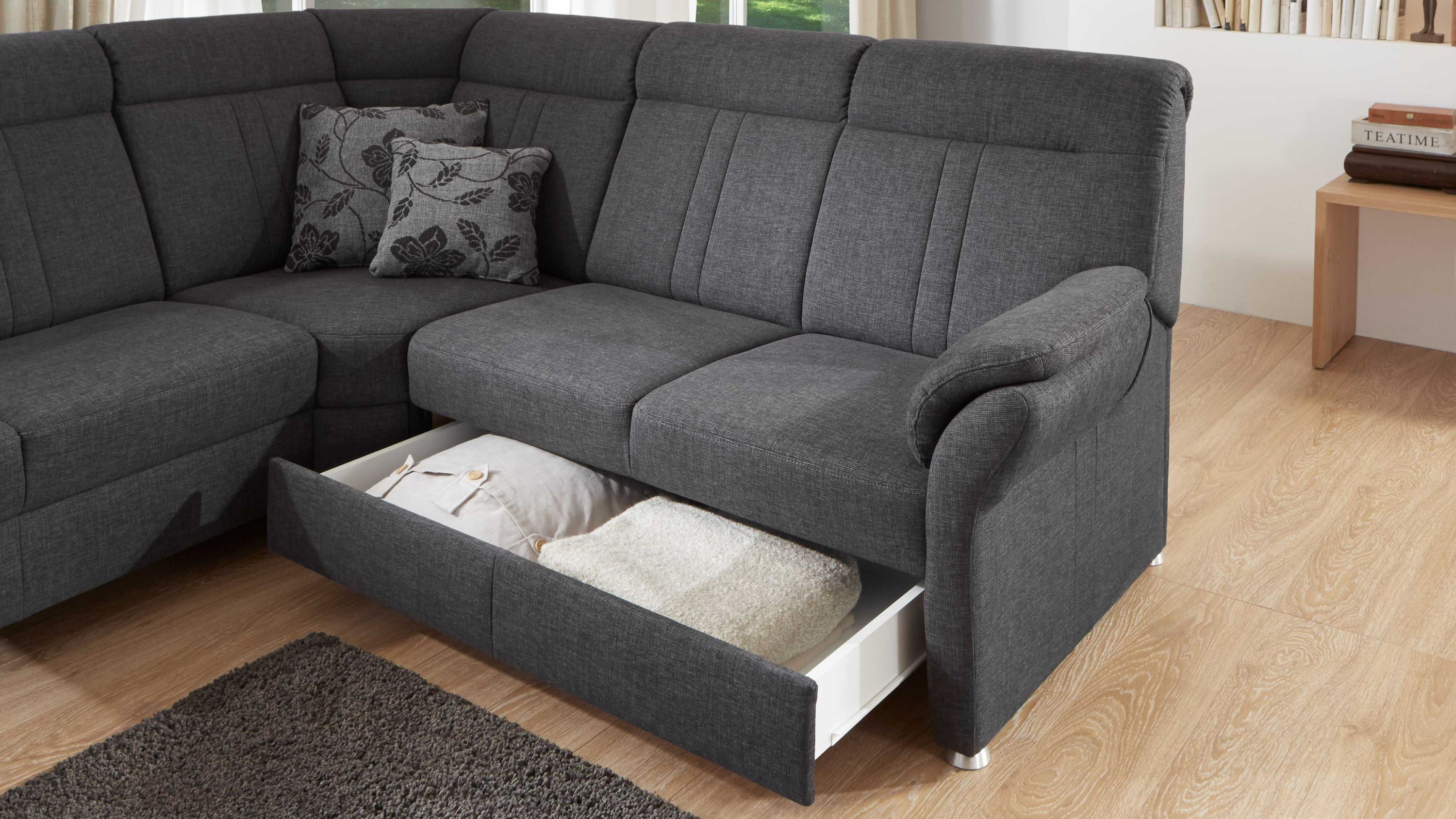 Ecksofa in dunkelgrauem Stoff mit Bettkasten unter der Sitzfläche gefüllt mit Kissen und Decke
