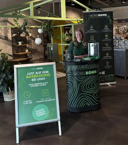 Infostand von Möbel Bohn in einem Möbelhaus mit Marleen Miess dahinter, die für Ausbildungs-Info-Gespräche wirbt.