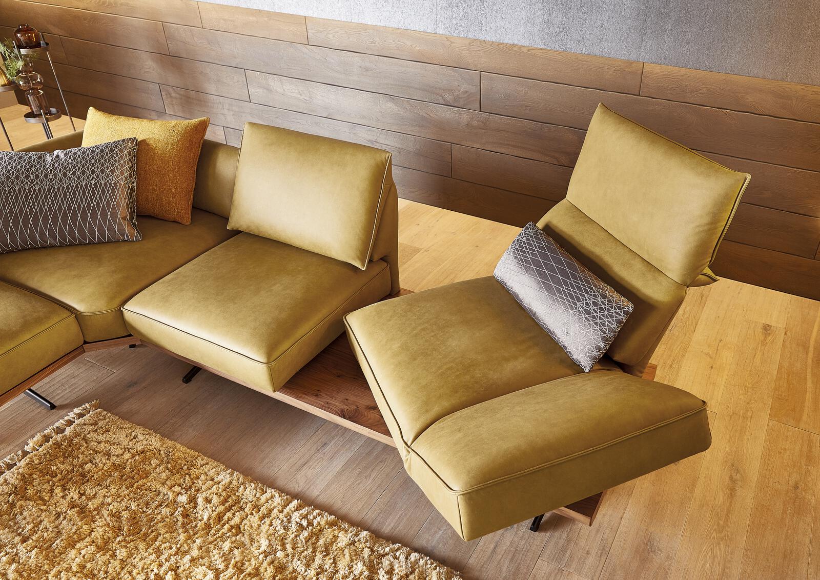 Modernes senfgelbes Ledersofa von Koinor mit Holzablage, verstellbaren Sitzelementen und dekorativen Kissen.
