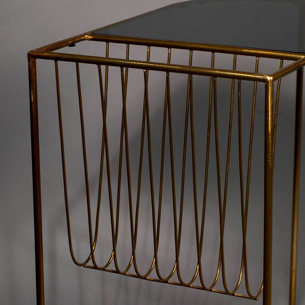 Beistelltisch goldenes Metallgestell mit schwarzer Glasplatte Detailaufnahme eines Beistelltischs mit goldenem Metallgestell und schwarzer Glasplatte vor grauem Hintergrund