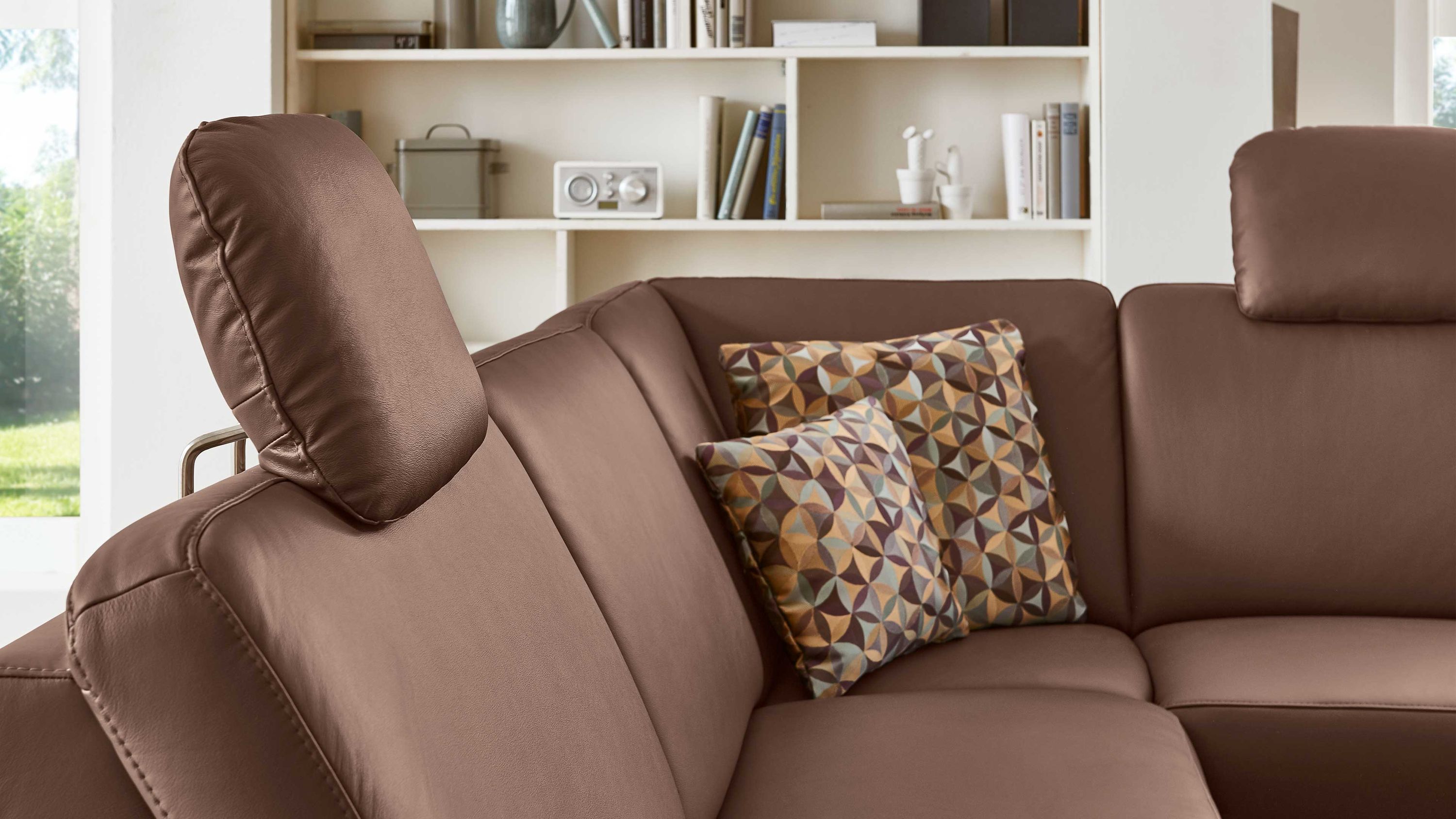 Ecksofa mit braunen Kopfstützen aus Leder Ecksofa mit zwei gemusterten Kissen und verstellbaren Kopfstützen in braunem Leder
