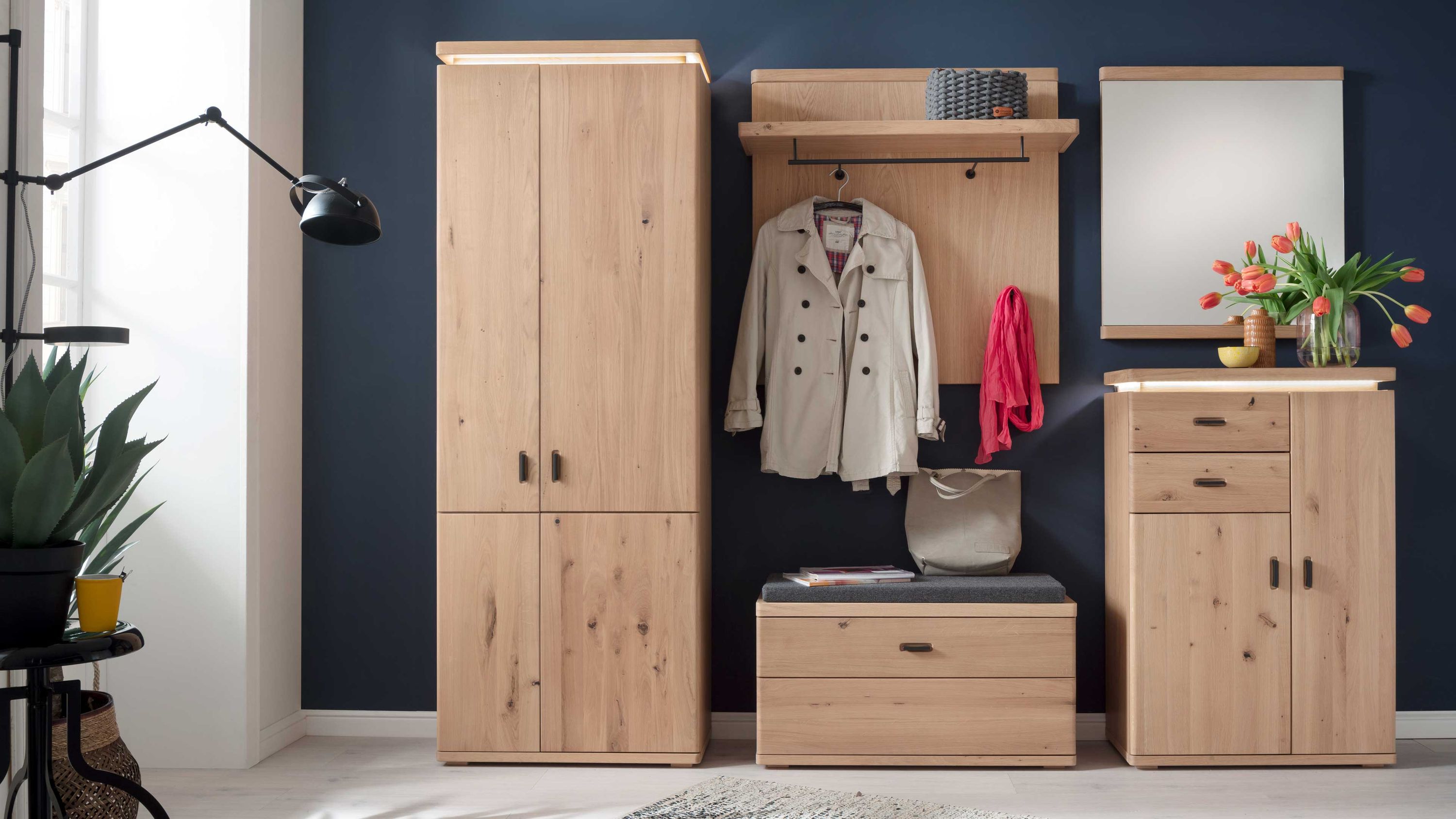 Fünfteiliges Garderobenprogramm aus hellem Holz mit Schrank Sitzbank Spiegel und Ablagen vor dunkelblauer Wand