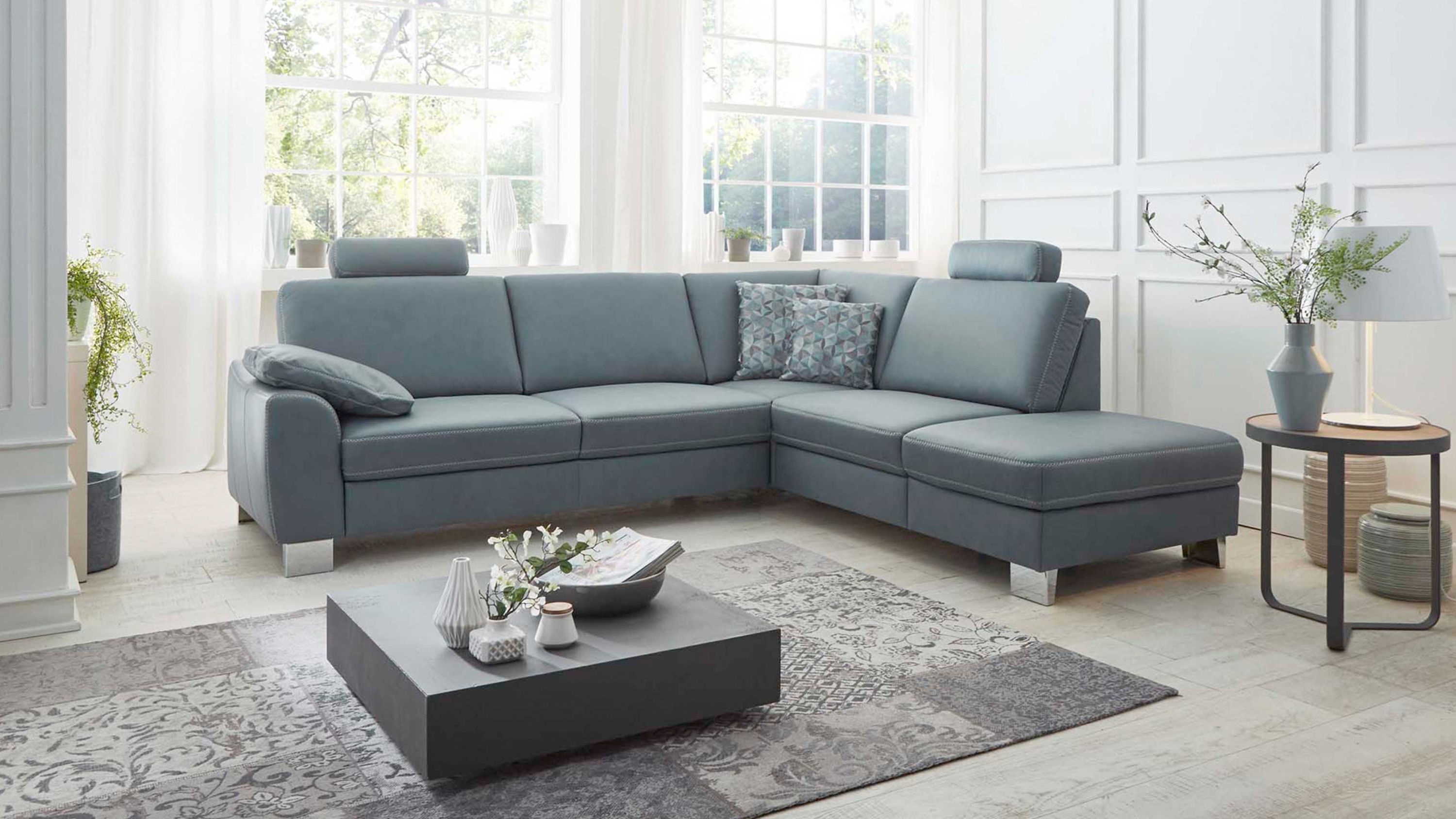 Ecksofa mit stahlfarbenem Lederbezug zwei Kopfstützen und Kissen in einem hellen Wohnzimmer