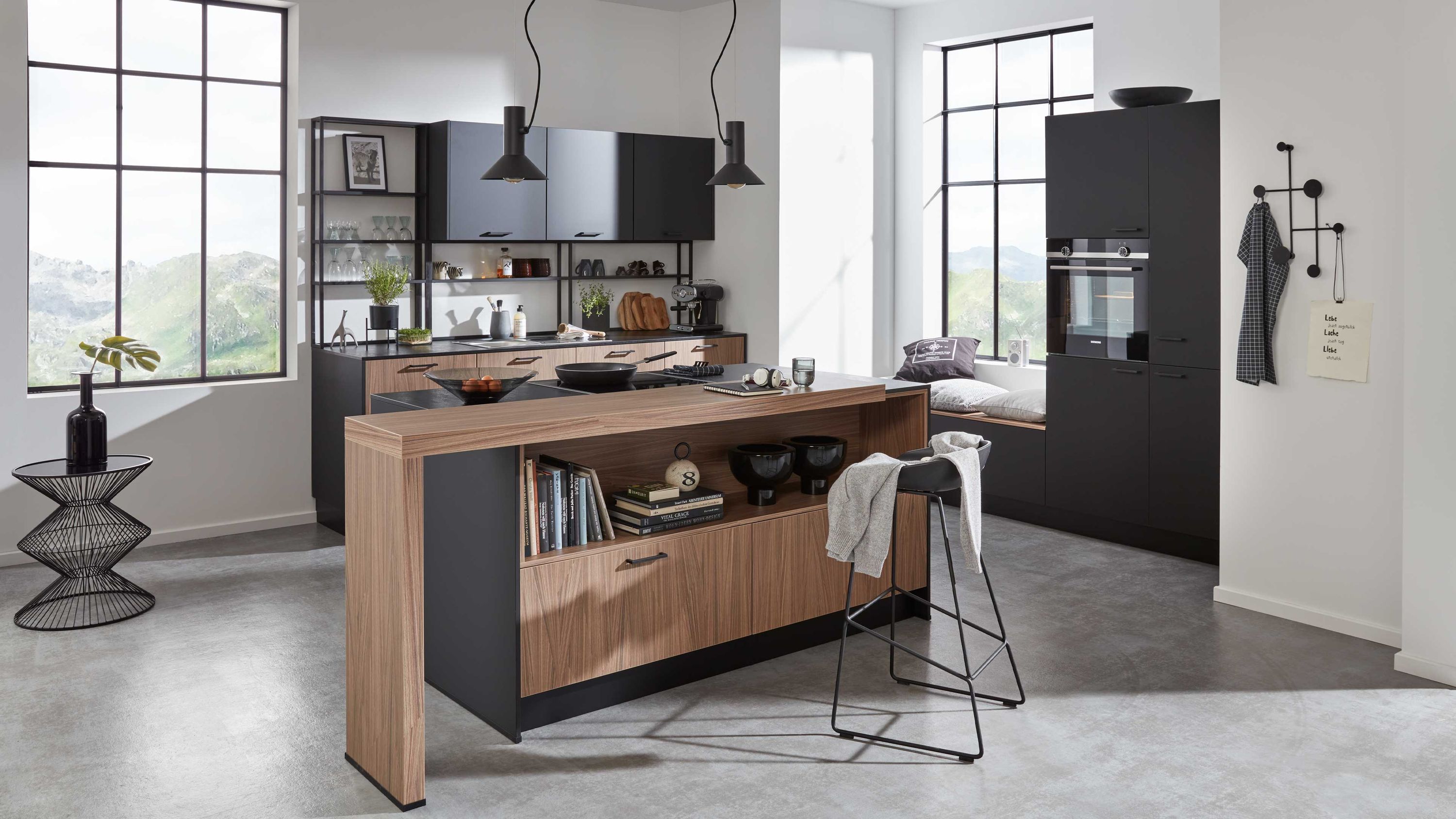 Zeitgemäße Küche mit Inseldesign offenen Stauraumlösungen und natürlichem Lichteinfall Küche mit Holz-Schwarz-Insel offenen Regalen Hängelampen Barhocker Fensterlicht moderne Linienführung
