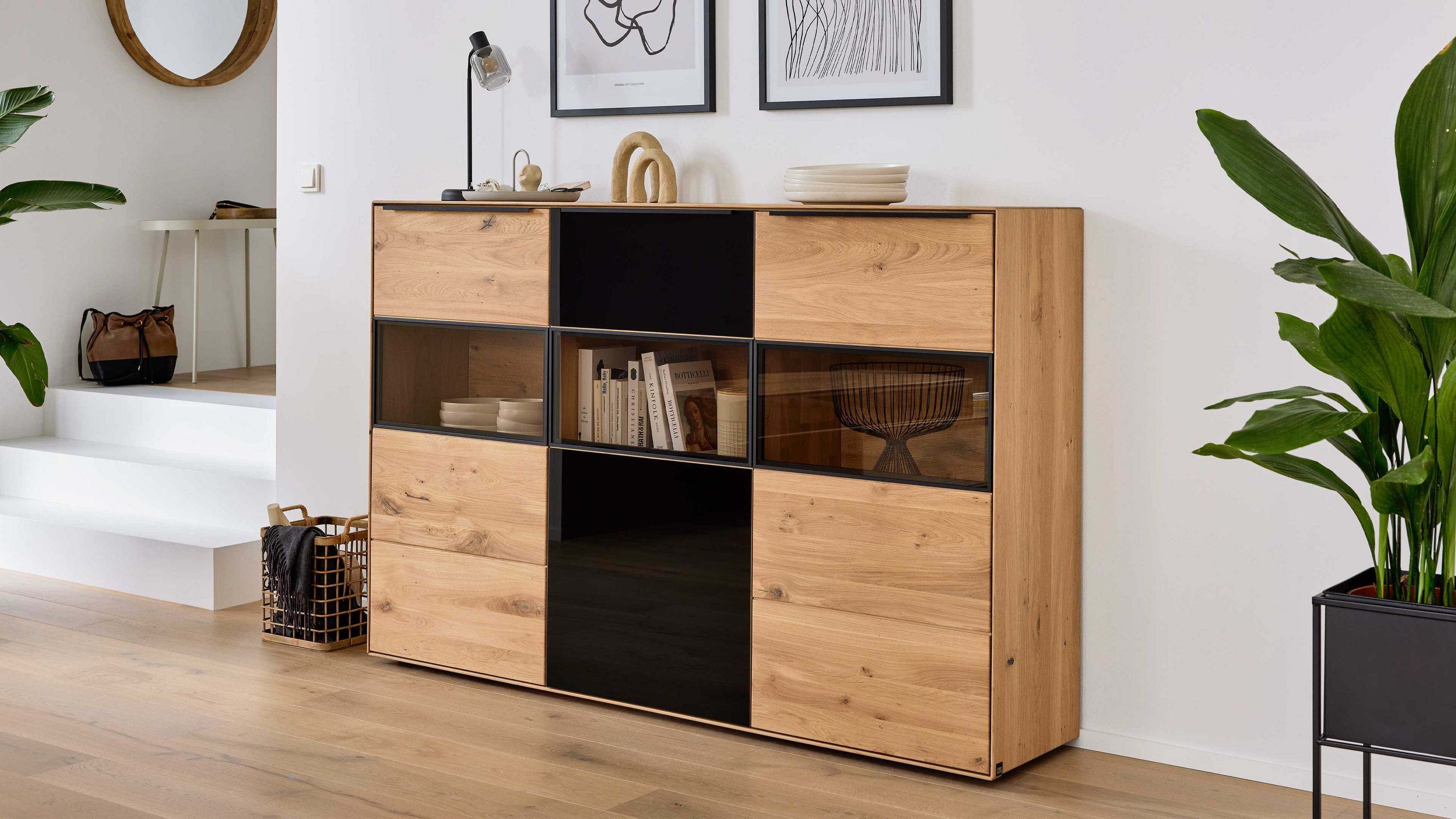 Highboard mit Holz und Glasfronten Highboard mit drei Türen aus hellem Holz und dunklen Glaseinsätzen in einem modernen Wohnzimmer
