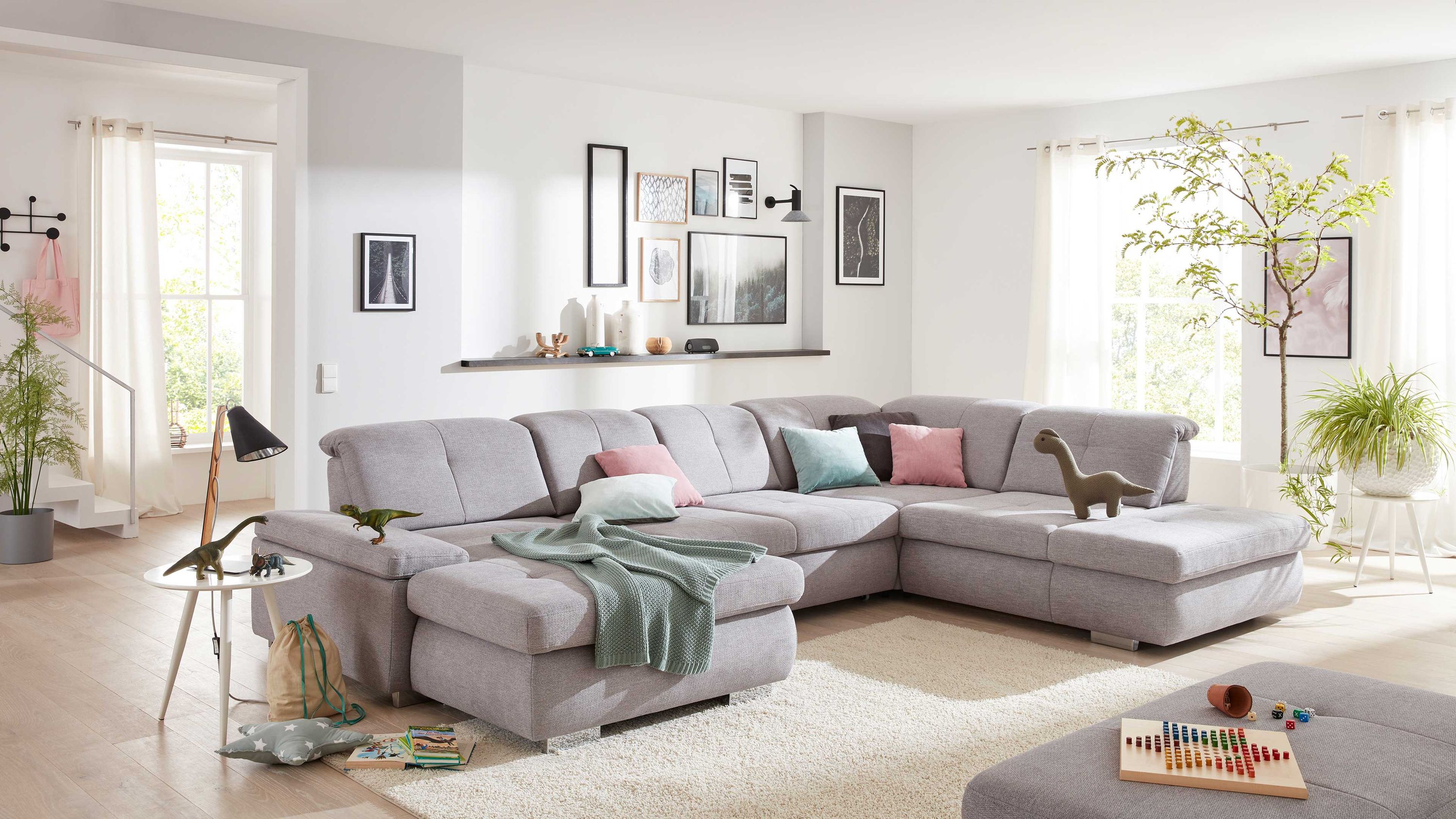 Große silberfarbene Wohnlandschaft mit Metallfüßen und mehreren bunten Kissen in hellem Wohnzimmer