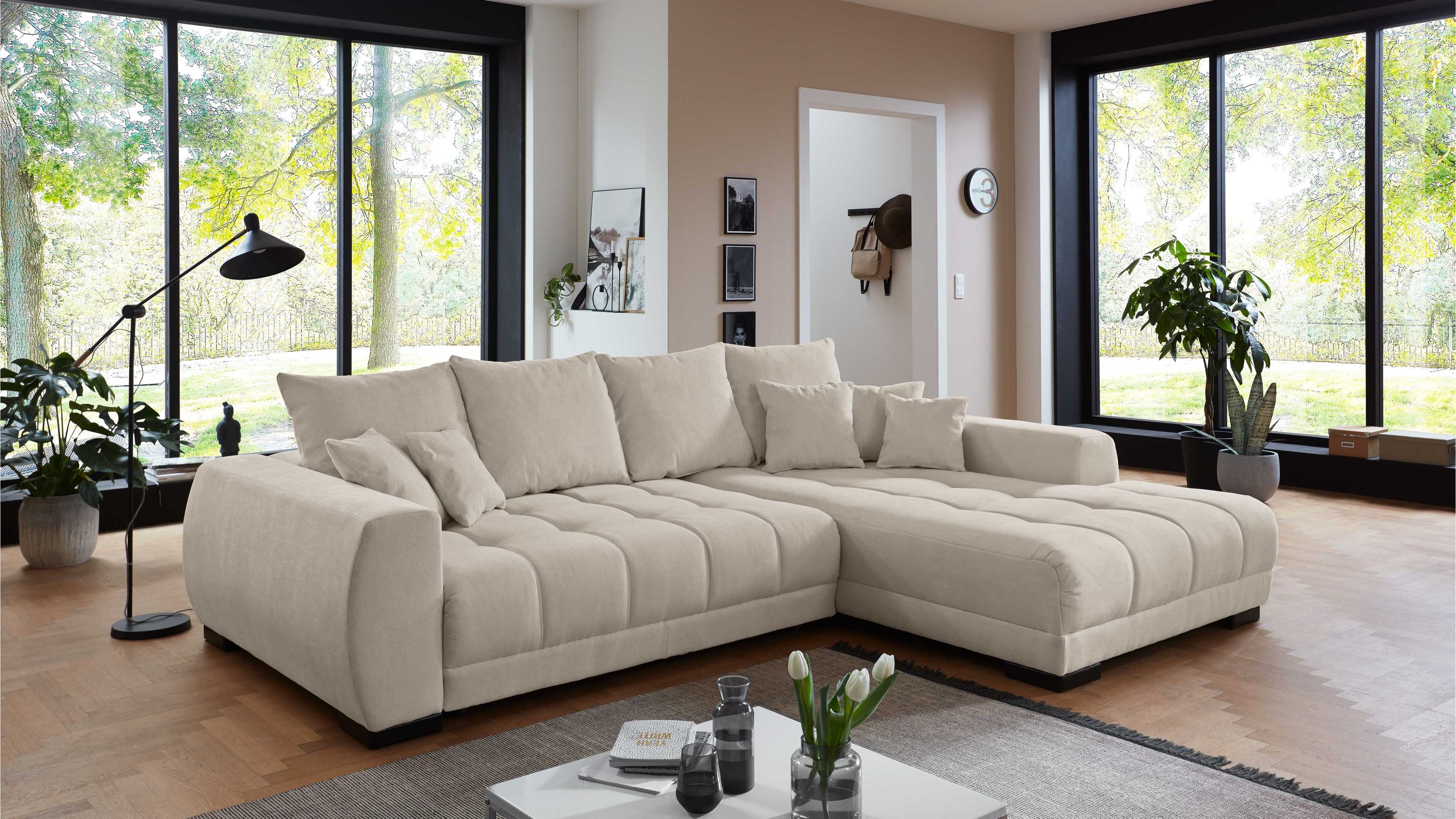 Beige Eckcouch mit breiten Armlehnen gepolsterten Sitzflächen und schwarzen Füßen in modernem Wohnzimmer