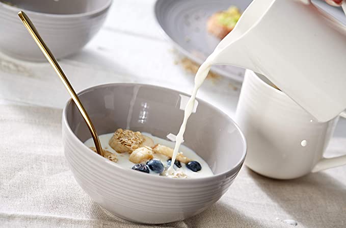 Frisches Müsli mit Milch in Szene gesetzt Seitliche Nahaufnahme: Milch wird aus Krug in Müslischüssel mit goldenem Löffel gegossen.