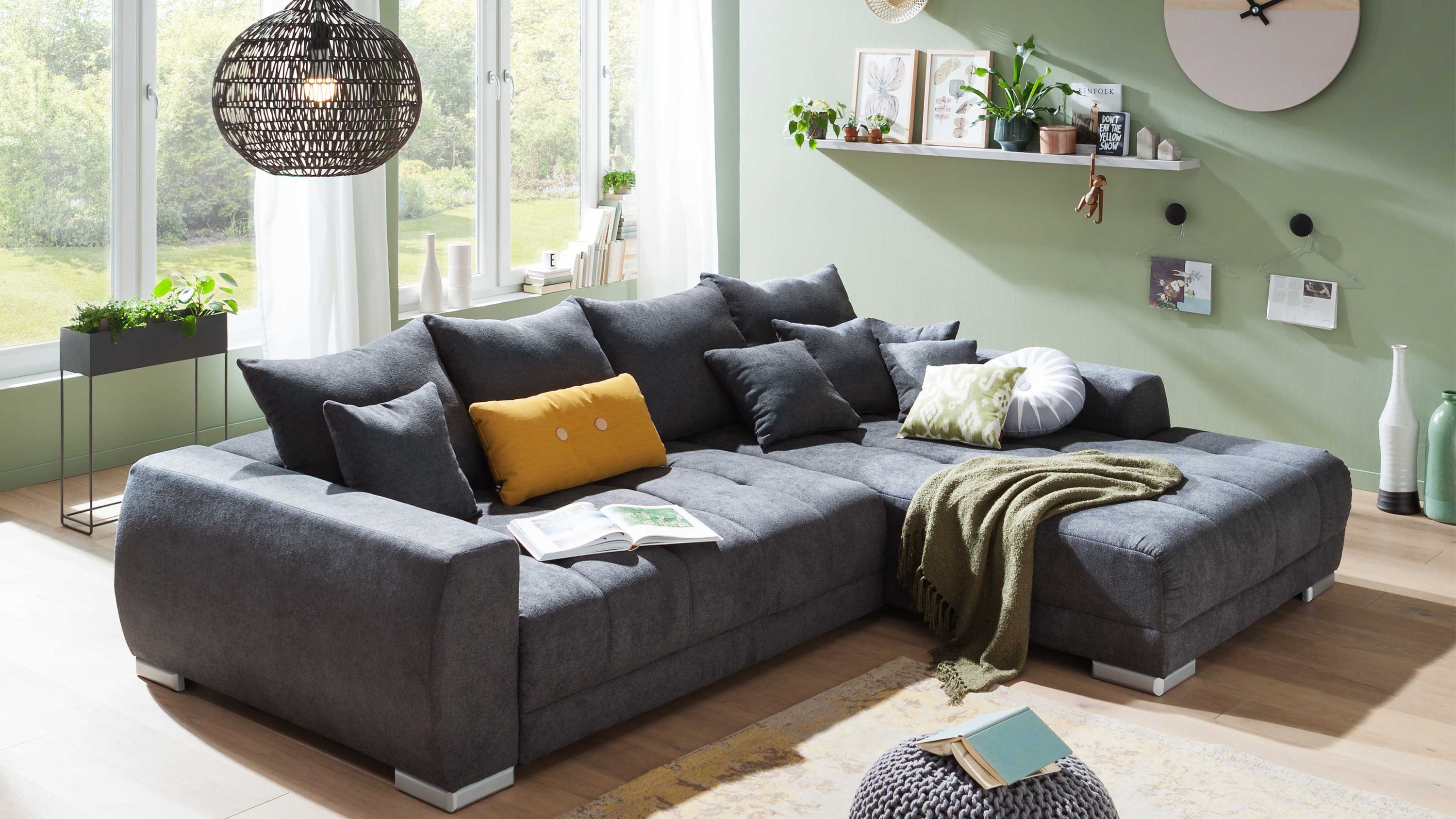 Dunkelgraue Eckcouch mit mehreren Kissen und einem gelben Zierkissen in modernem Wohnzimmer