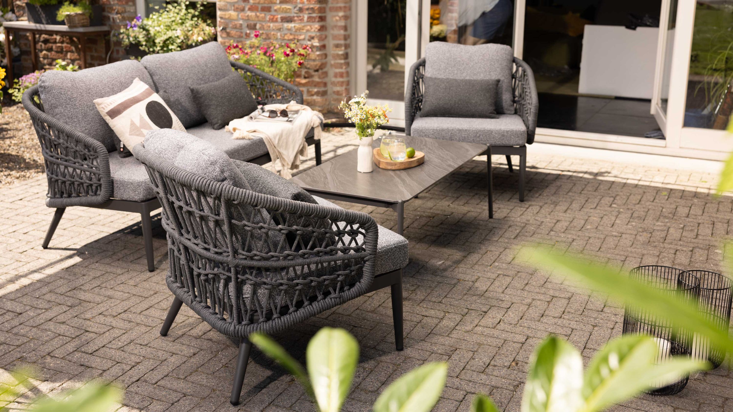 Dreiteiliges Loungemöbel-Set mit grauen Polstern und Rope-Geflecht auf Aluminiumrahmen auf gepflasterter Terrasse