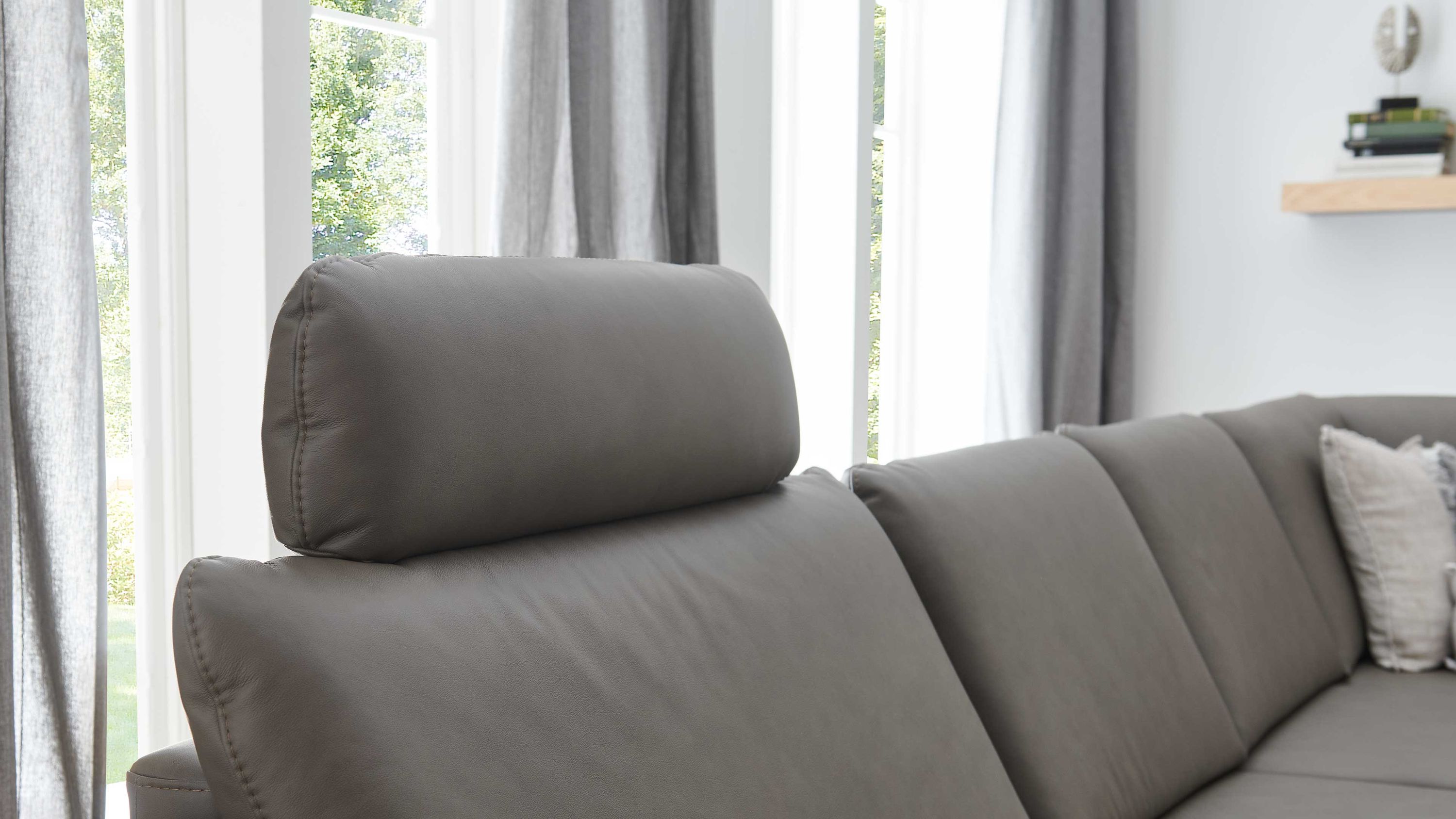 Steingraue Kopfstütze aus Leder auf einem grauen Sofa in einem hellen Raum