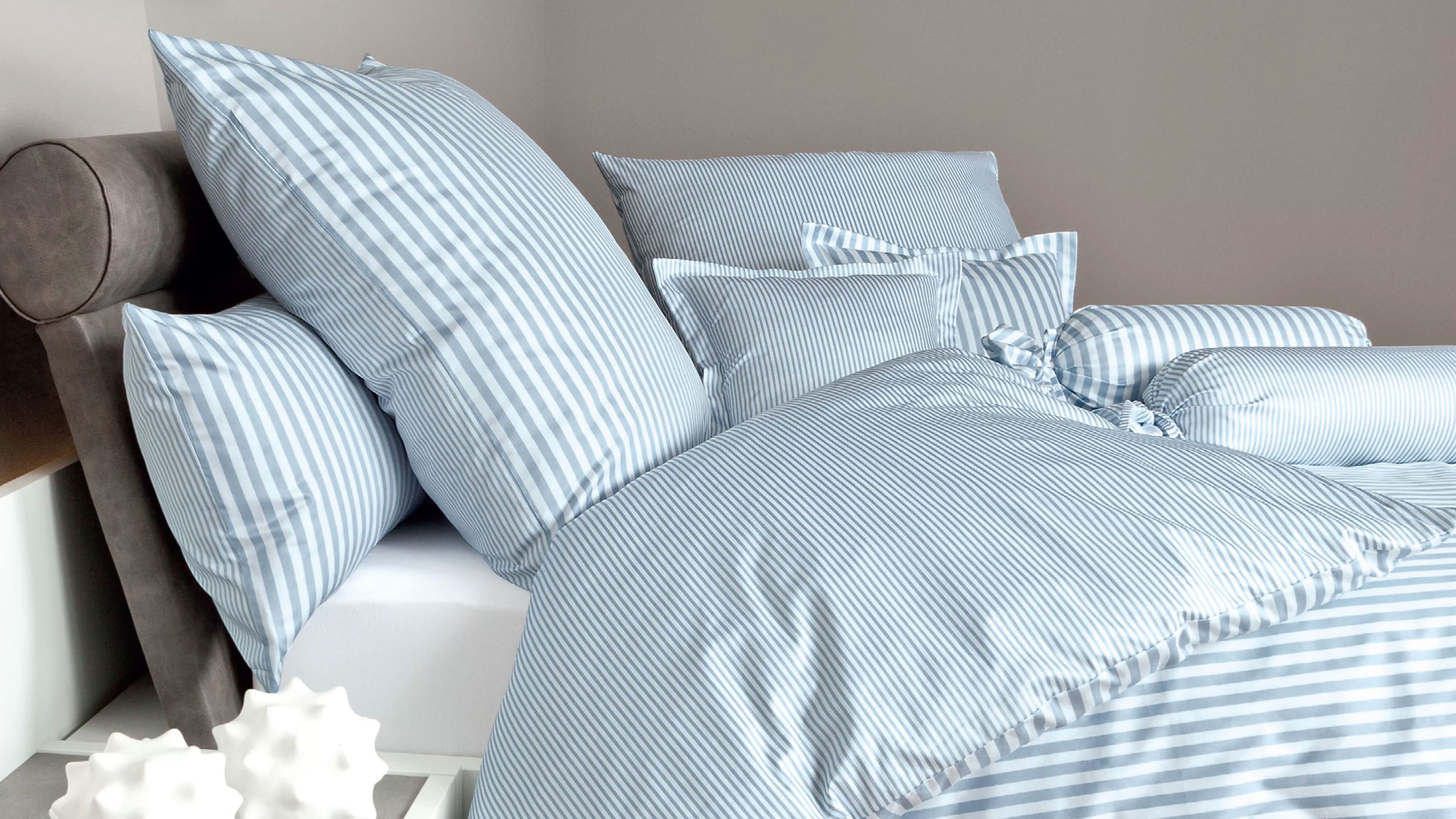 Bett mit gestreifter Bettwäsche in weiß und blau mit mehreren Kissen und Nackenrollen