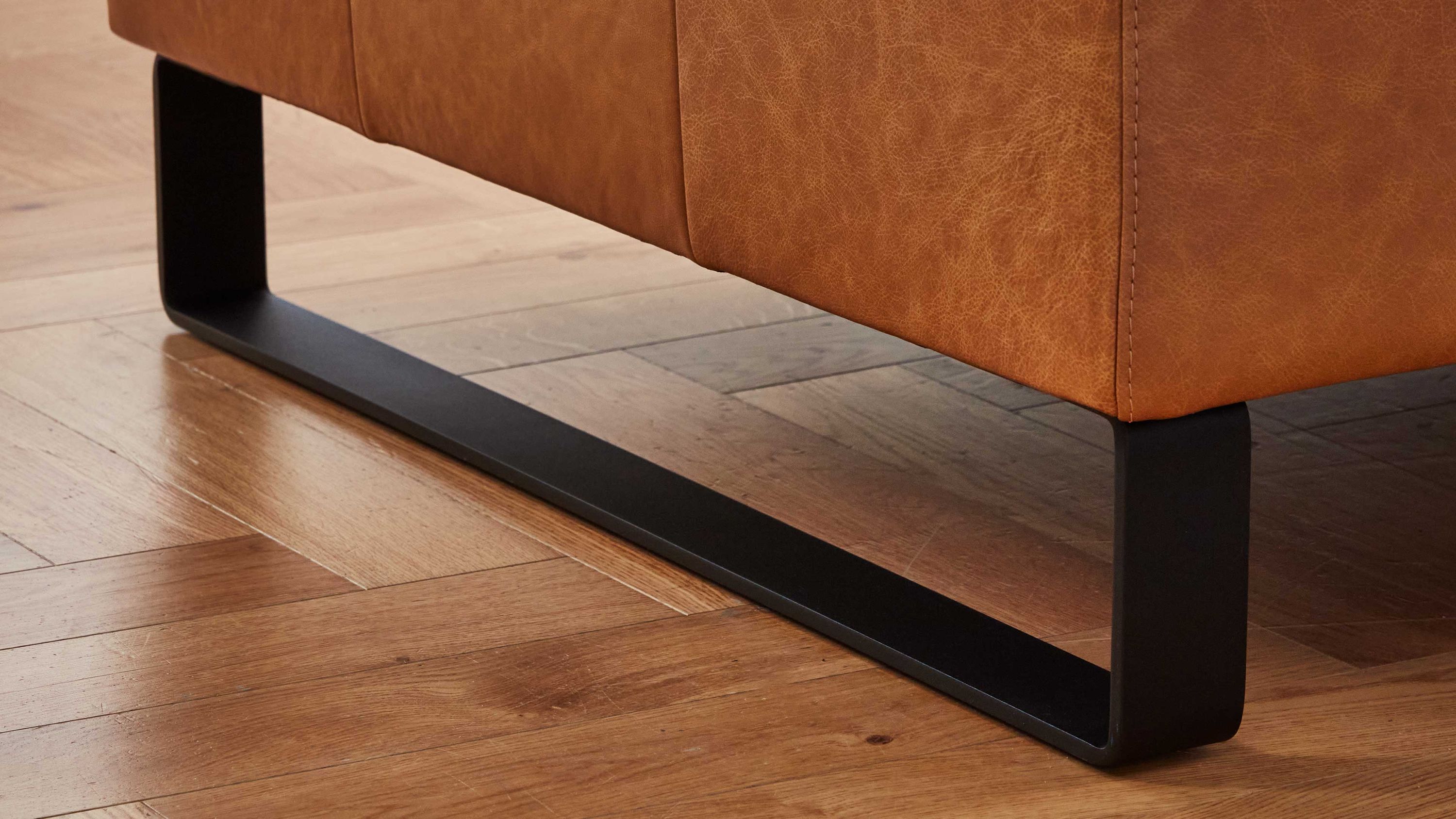 Sofafuß aus schwarzem Metall in Kufenform Schwarze Metallkufe als Fuß eines braunen Sofas auf Holzboden