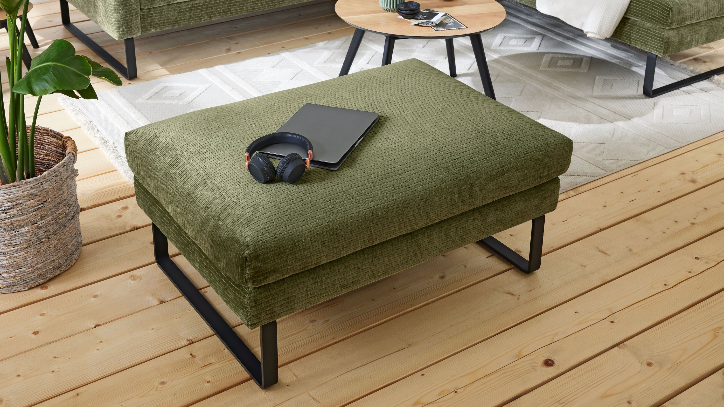 Rechteckiger Polsterhocker mit grünem Bezug und schwarzen Kufenfüßen Rechteckiger Polsterhocker mit grünem Bezug und schwarzen Kufenfüßen auf Holzboden