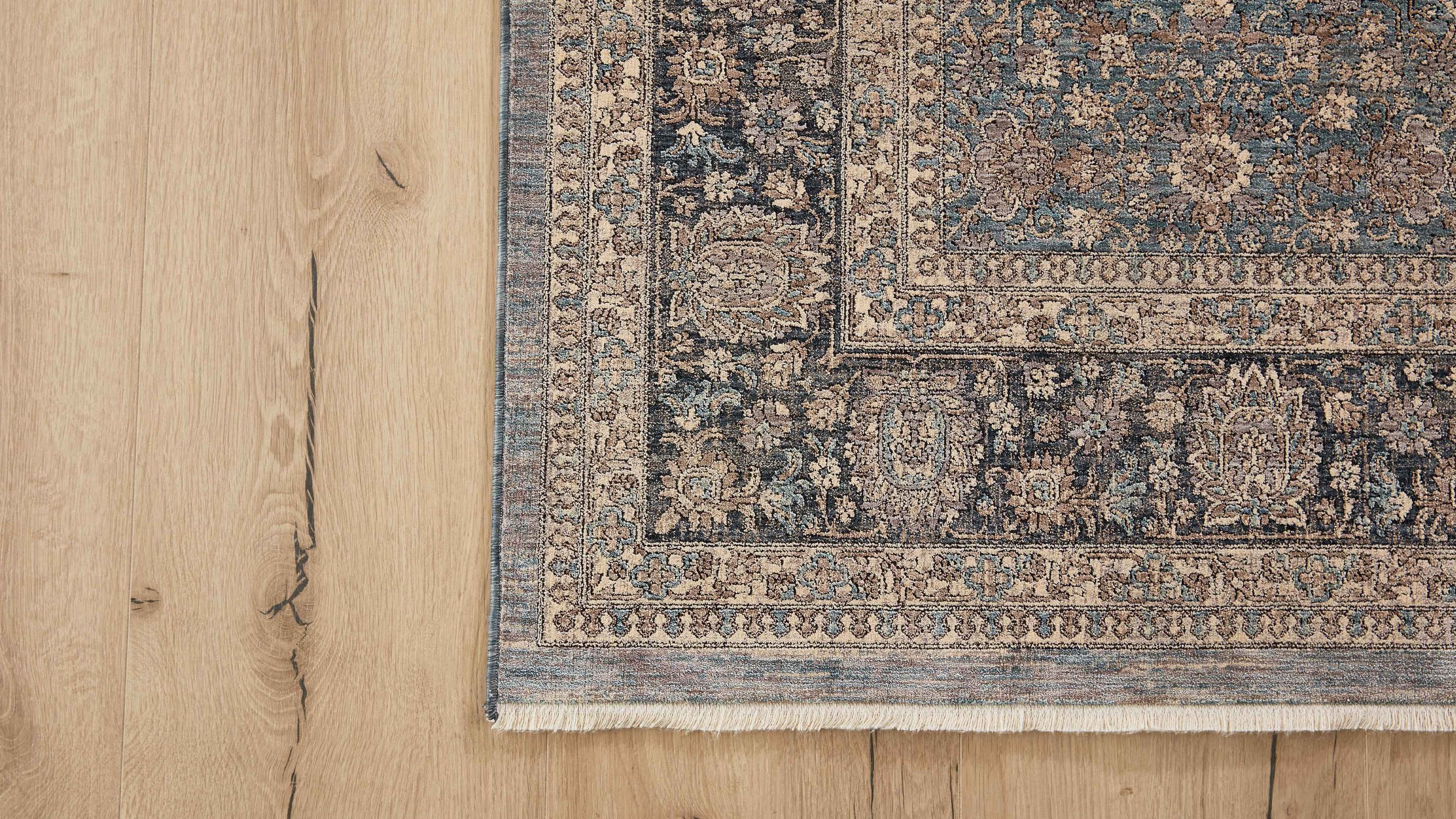 Blau gemusterter Teppich mit floralem Design und Fransen an der Kante auf hellem Holzboden