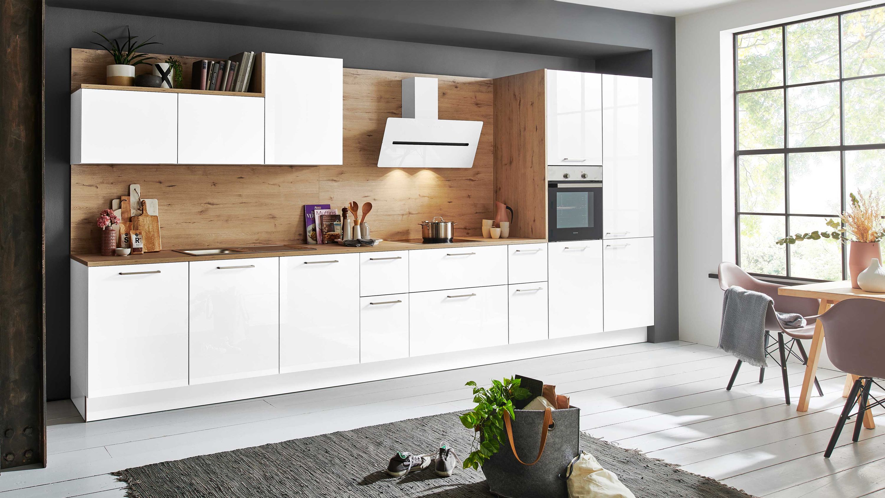 Weiße Küchenzeile mit Holzrückwand und Hängeschränken. Weiße Küchenzeile mit Holzrückwand Hängeschränken Dunstabzugshaube Einbauofen und großem Fenster.