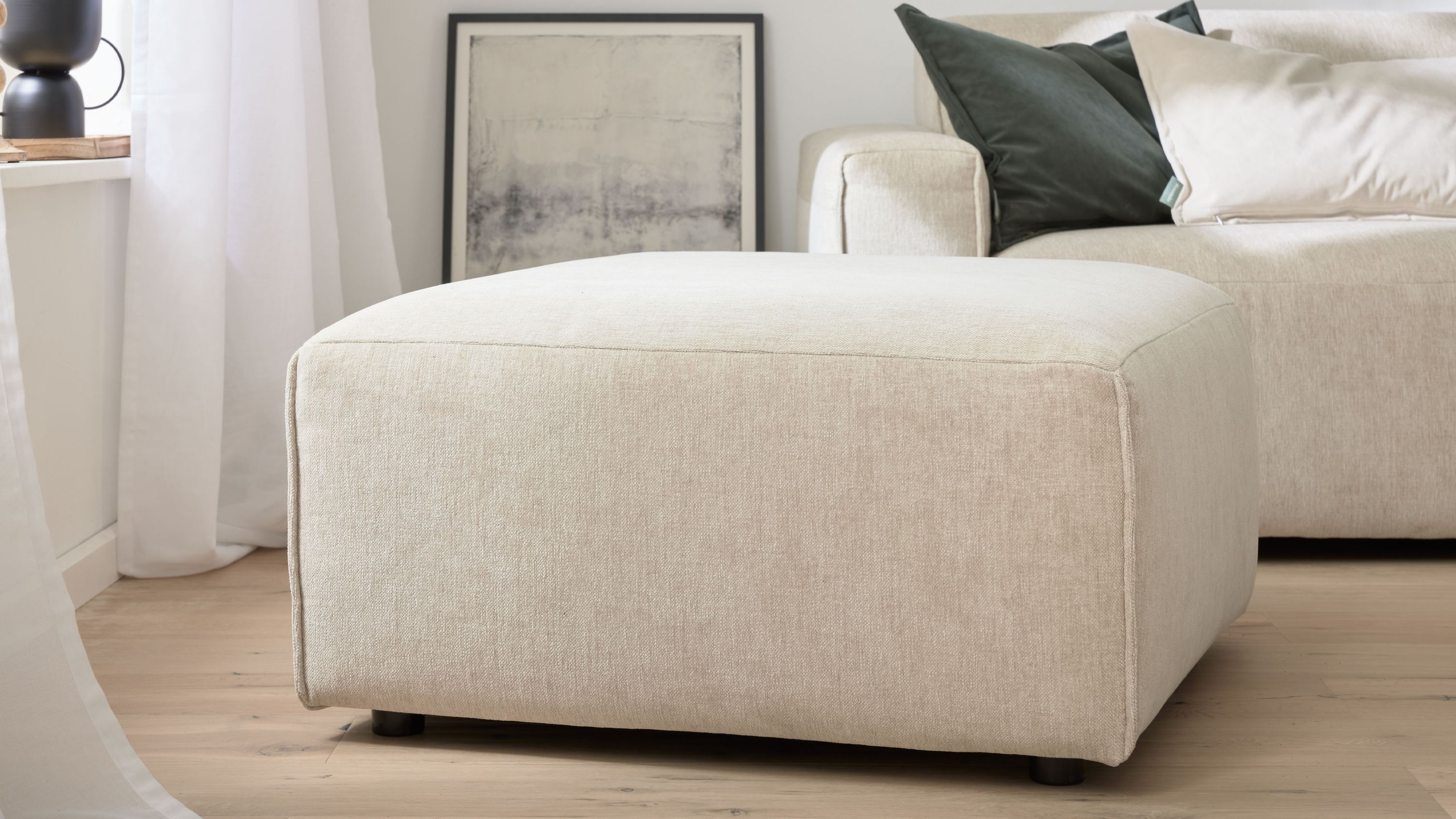 Quadratischer weißer Polsterhocker Großer quadratischer Polsterhocker in weiß mit glattem Stoffbezug auf Holzfußboden vor Sofa