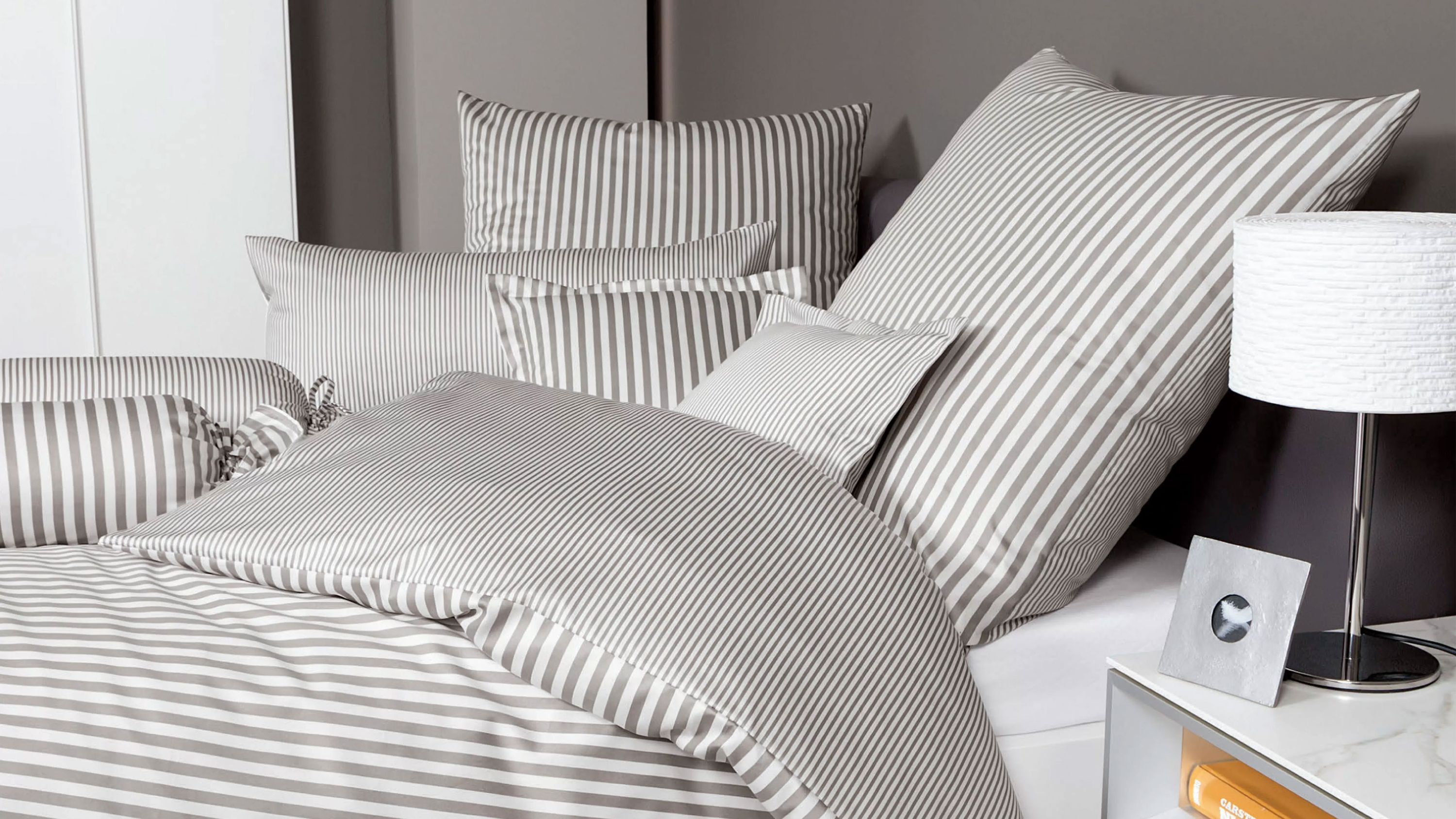 Bett mit mehrteiliger Bettwäsche in weiß und grauen Streifen auf Kissen und Decke
