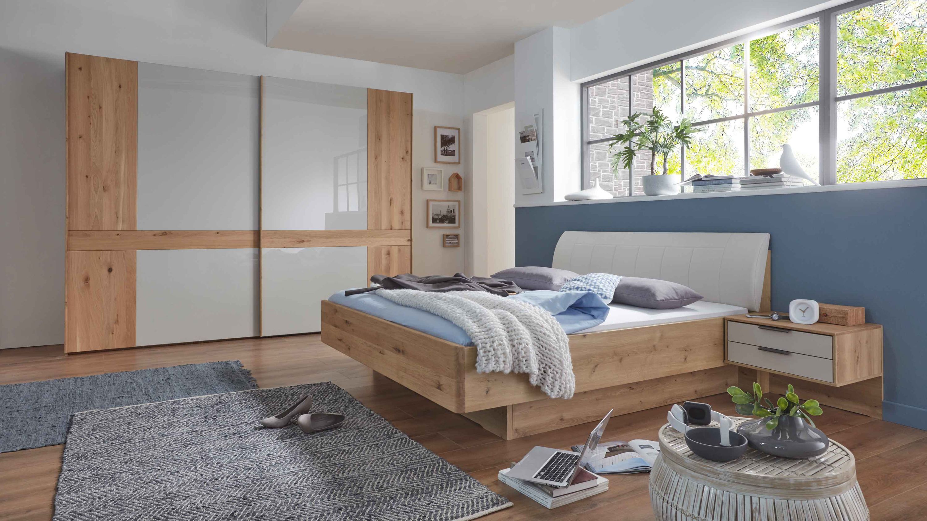 Schlafzimmer mit Bett und Nachttisch in Holzoptik und großem Kleiderschrank mit hellen Fronten