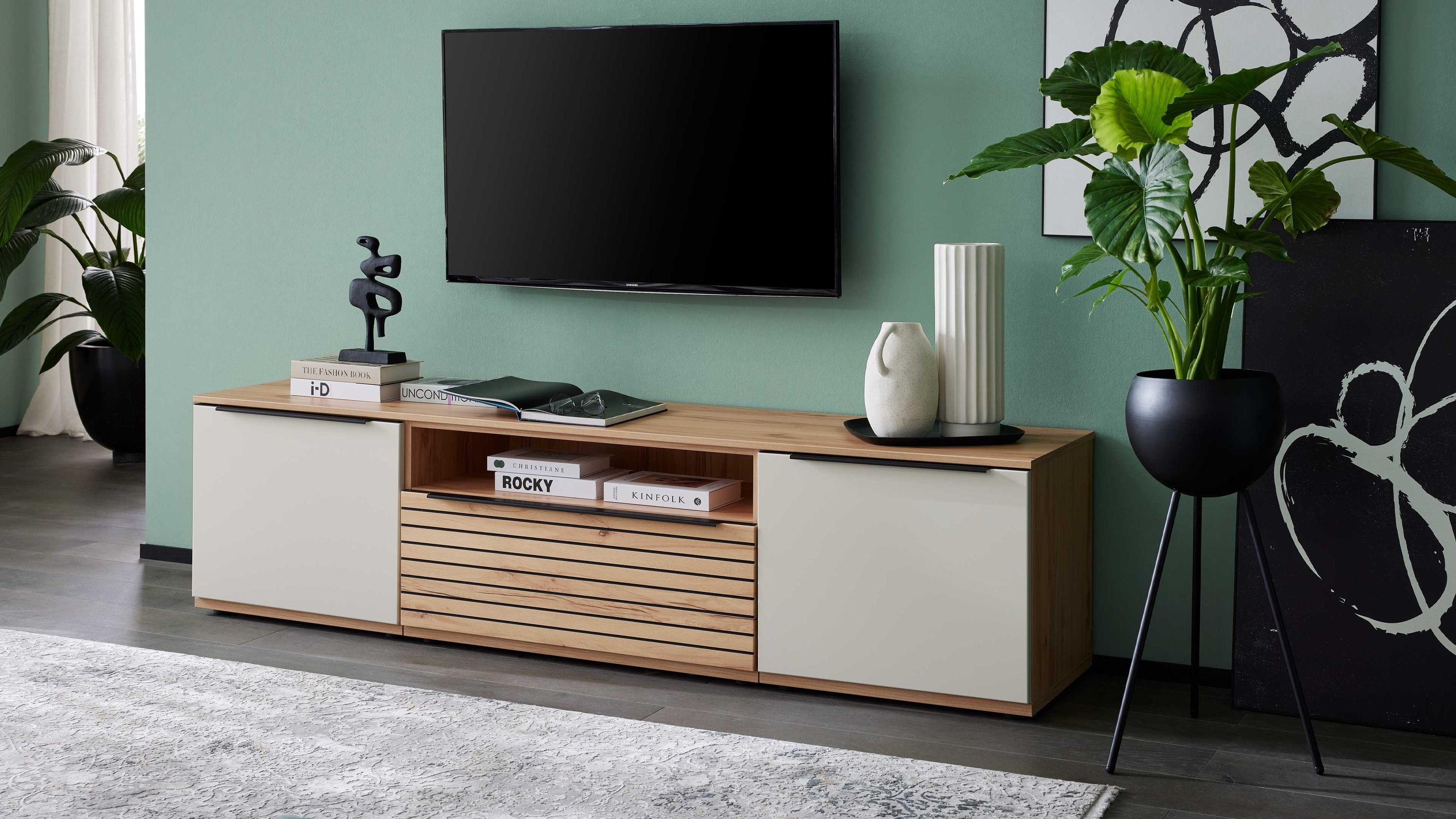 Dreiteiliges Lowboard in Sandbeige und Balkenbuche Dreiteiliges Lowboard mit sandbeigen Türen und balkenbuchefarbenem Korpus unter einem an der Wand montierten Fernseher
