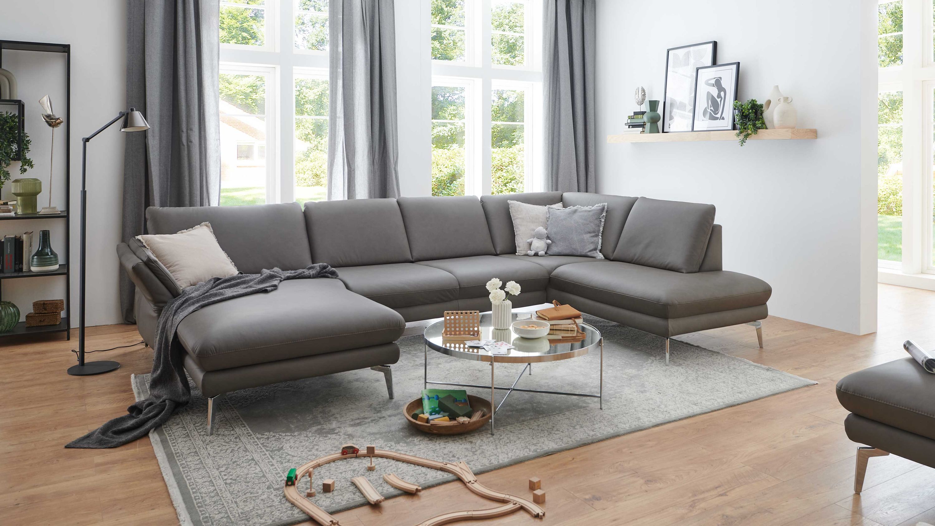 Wohnlandschaft steingrau mit Metallfüßen Große Wohnlandschaft in steingrau mit Metallfüßen in hellem Wohnzimmer mit Teppich und Couchtisch