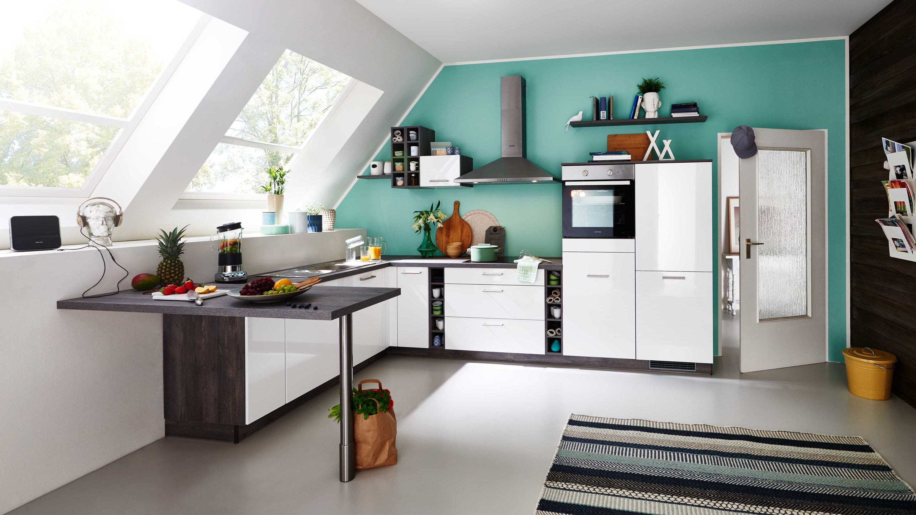 Küche mit weißen Schränken Schräge mit Fenstern türkisfarbener Wand Teppich Geräten und Dekorelementen