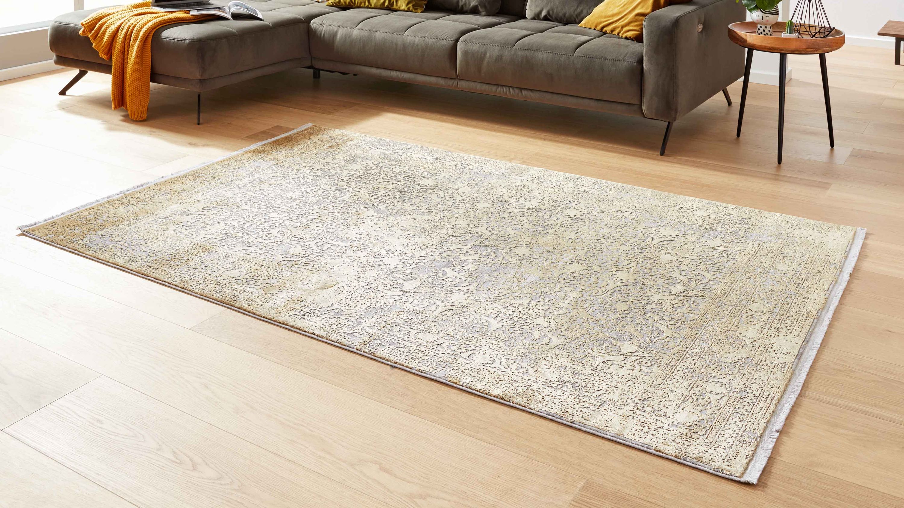 Rechteckiger Teppich mit feinem Muster in hellen Beige- und Goldtönen auf hellem Holzboden