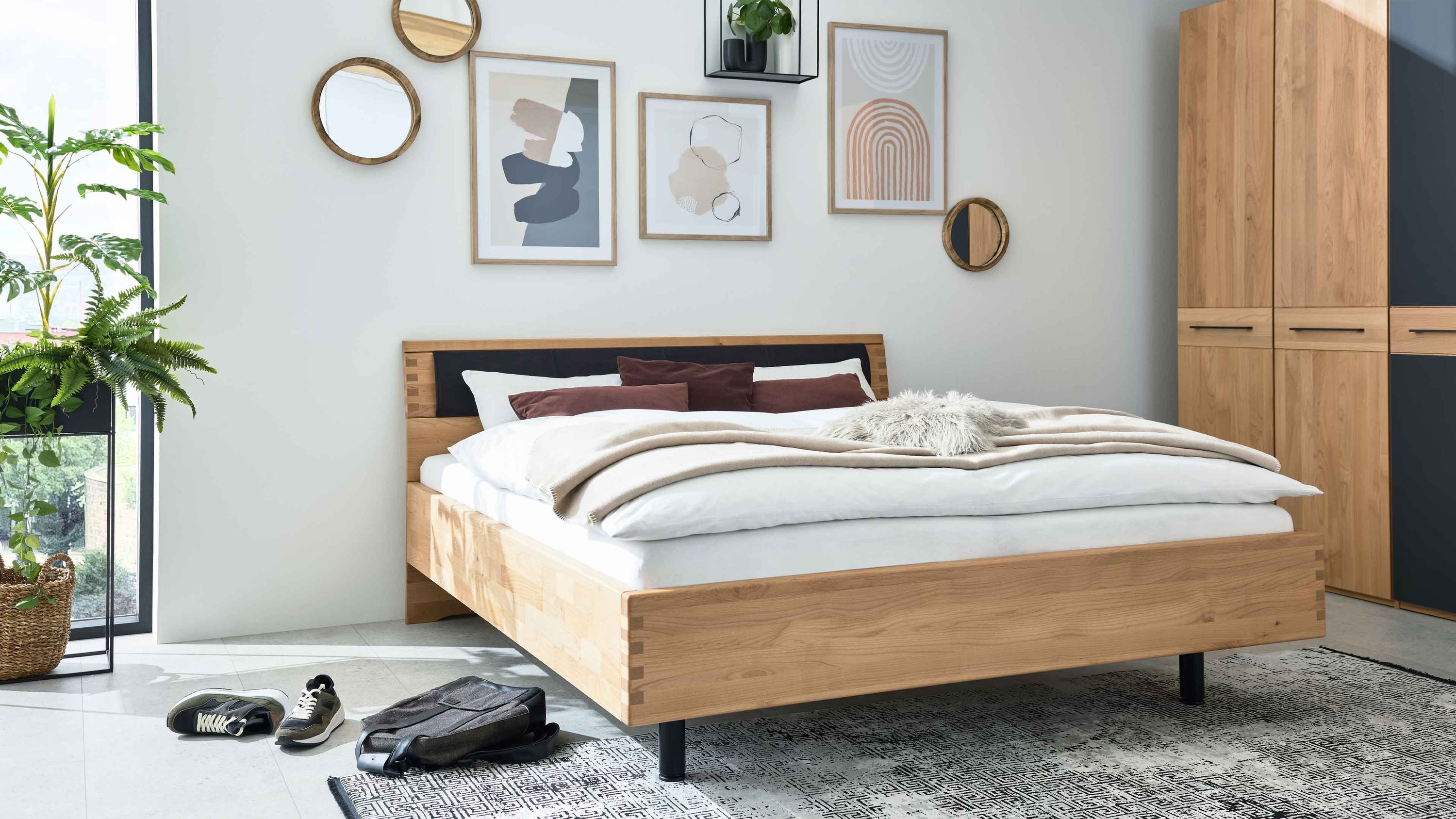 Bettgestell aus hellem Holz mit schwarzem gepolstertem Kopfteil in modernem Schlafzimmer