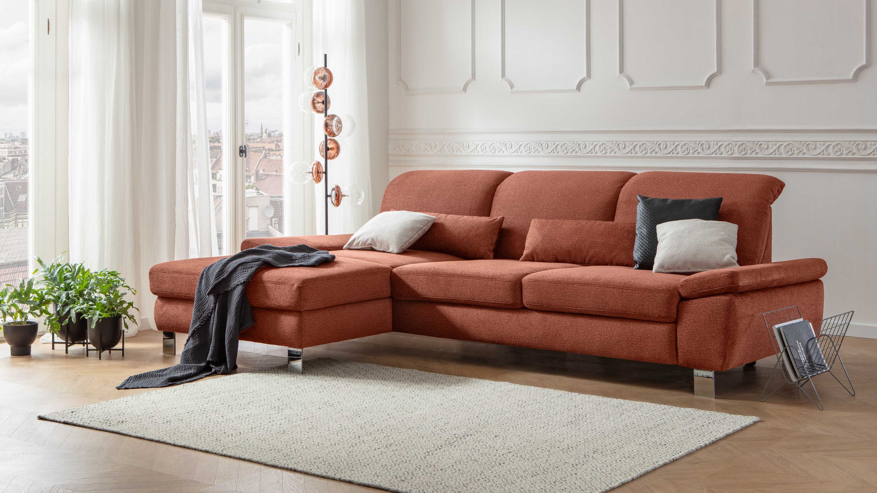 Ecksofa mit kupferfarbenem Stoffbezug und schwarzen Metallfüßen mit Kissen und Decke belegt