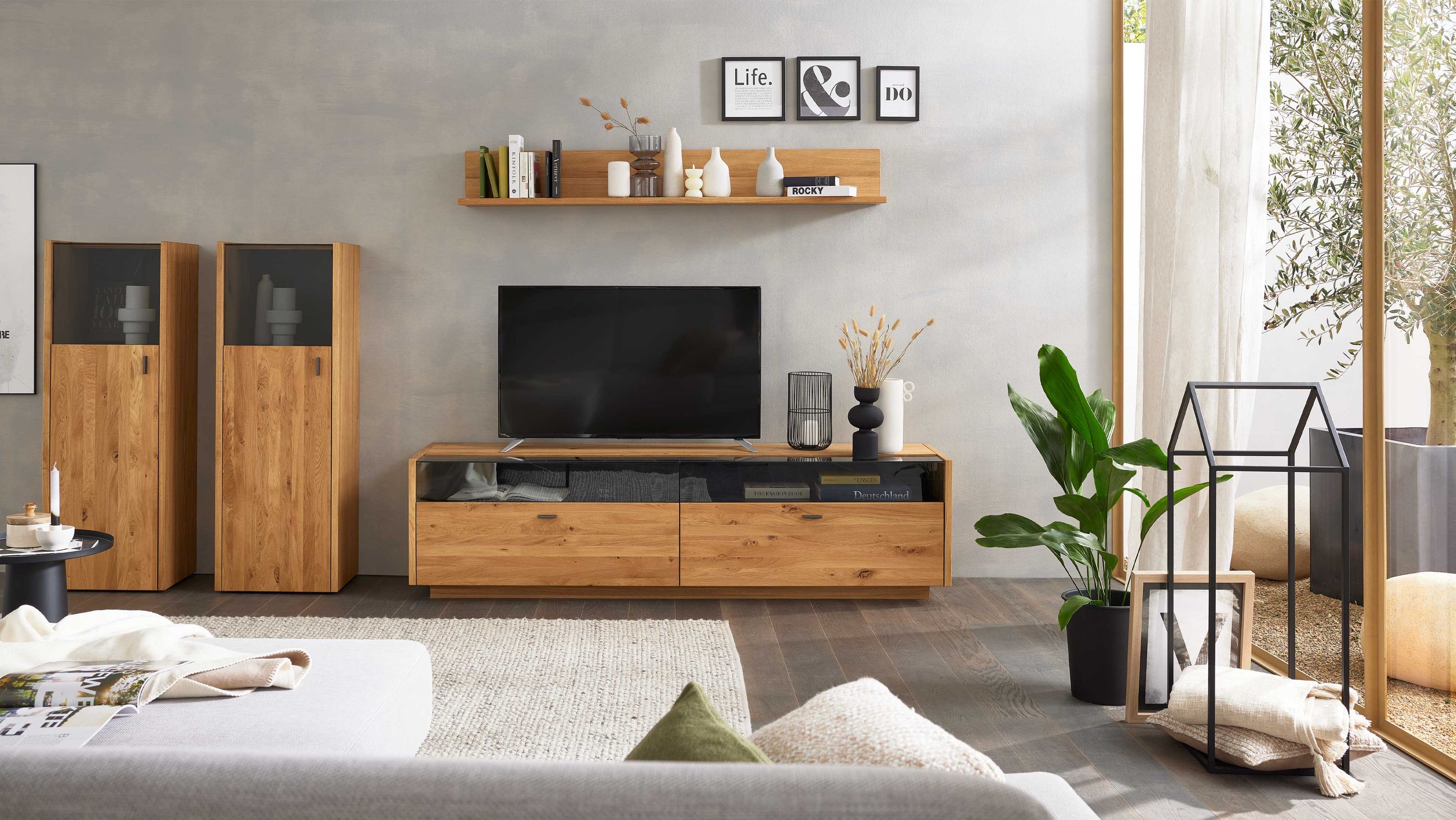 Vierteilige Wohnwand aus hellem Holz mit Vitrinen und TV-Board Vierteilige Wohnwand aus hellem Holz mit zwei hohen Vitrinen einem TV-Board und einem Wandregal mit Dekoration