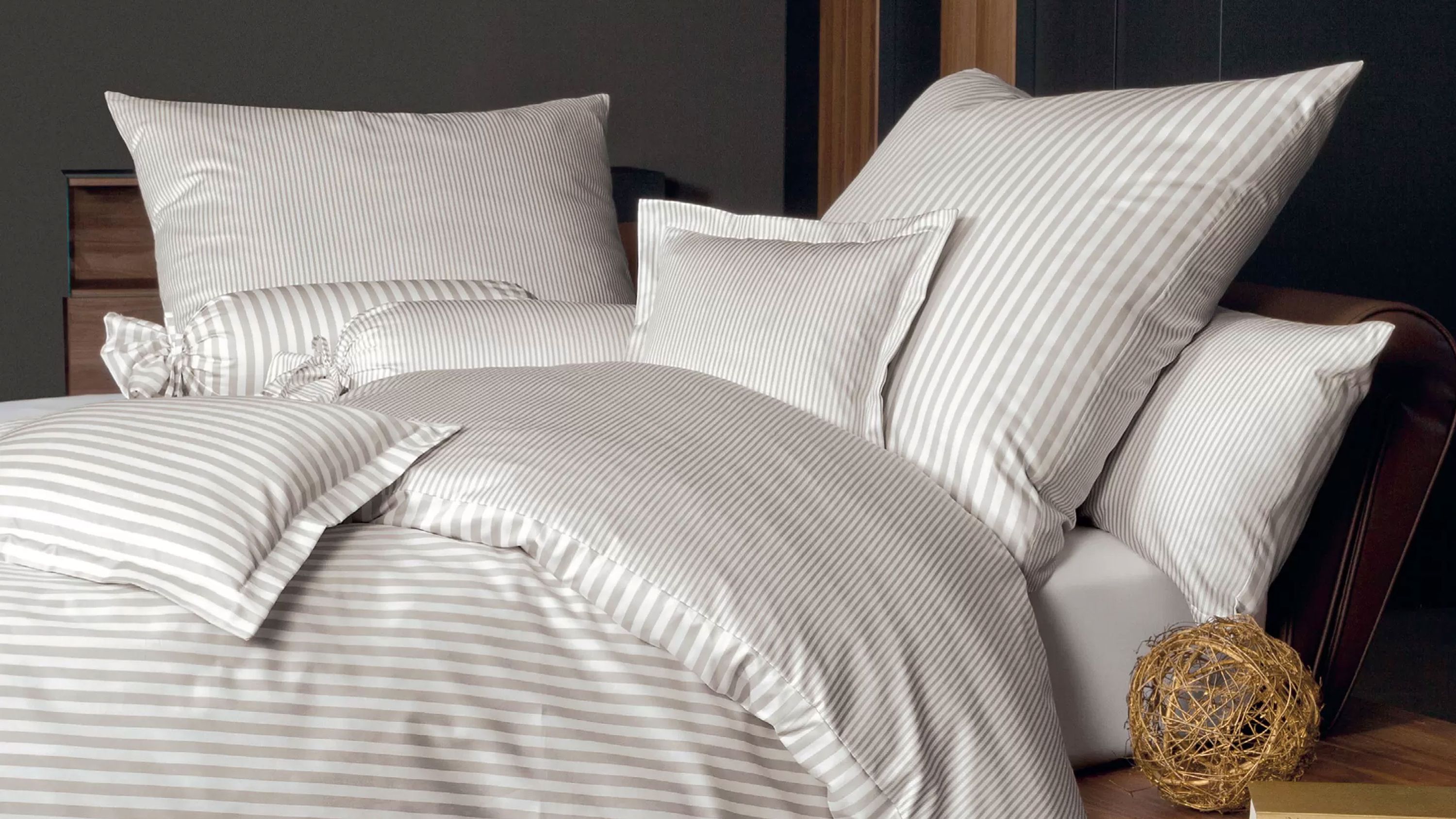 Bett mit gestreifter Bettwäsche und mehreren Kissen in hellen Farben