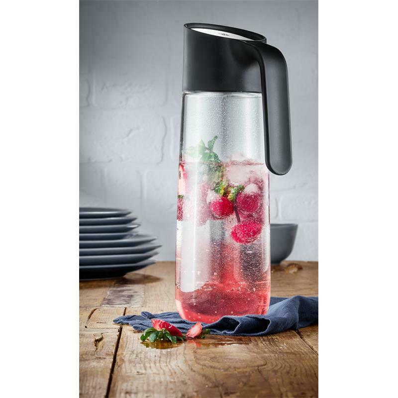  Schwarze Wasserkaraffe mit Griff  gefüllt mit Wasser  Früchten und Kräutern  auf Holzoberfläche platziert