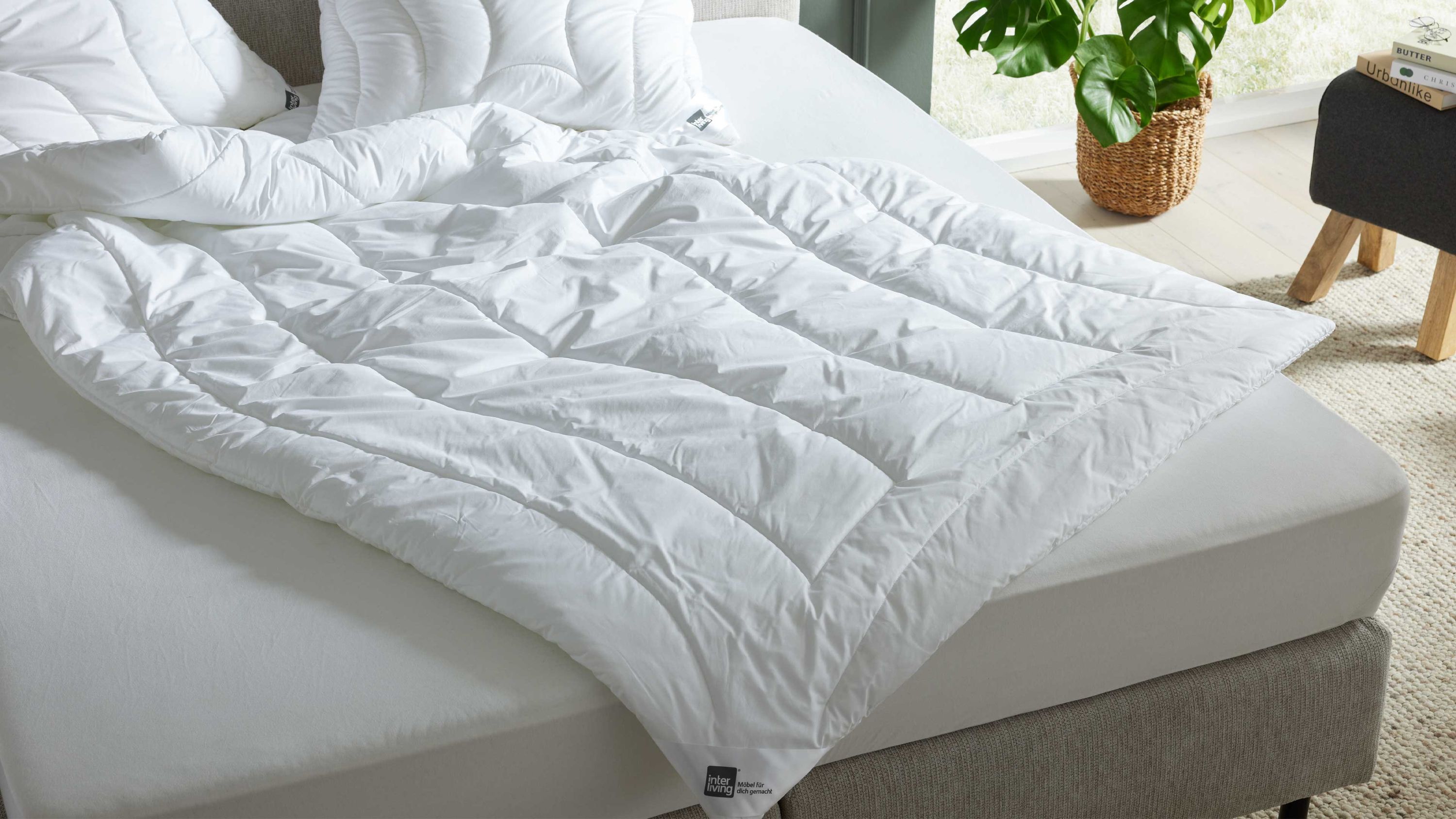 Weiße Bettdecke mit Steppmuster auf einem hellen Bett mit grauem Bettrahmen