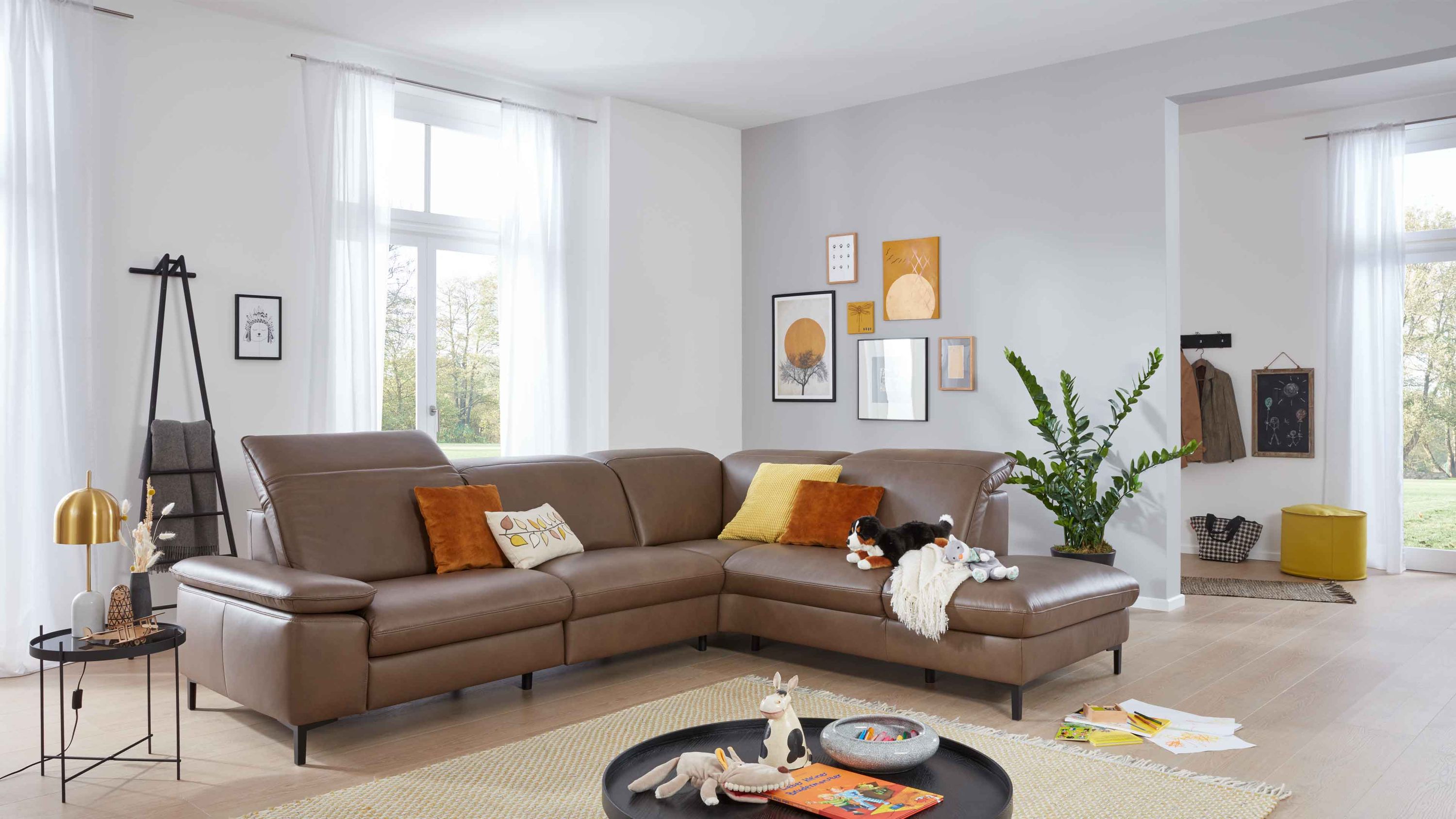 Ecksofa in steinfarbenem Leder mit schwarzen Metallfüßen in einem hellen Wohnzimmer