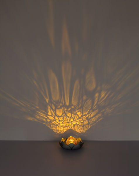 Leuchtende goldene Kugel in Blütenmitte mit dunklen Außen- und goldenen Innenblättern wirft Lichtmuster auf den Untergrund.