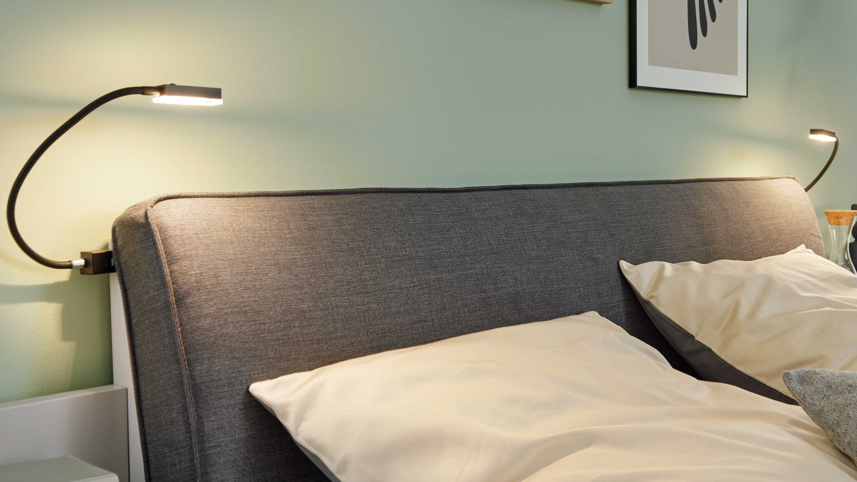 Flexleuchten-Set mit zwei flexiblen Leselampen am Bettkopfteil Zwei flexible Leselampen mit schwarzen Armen an einem grauen gepolsterten Bettkopfteil