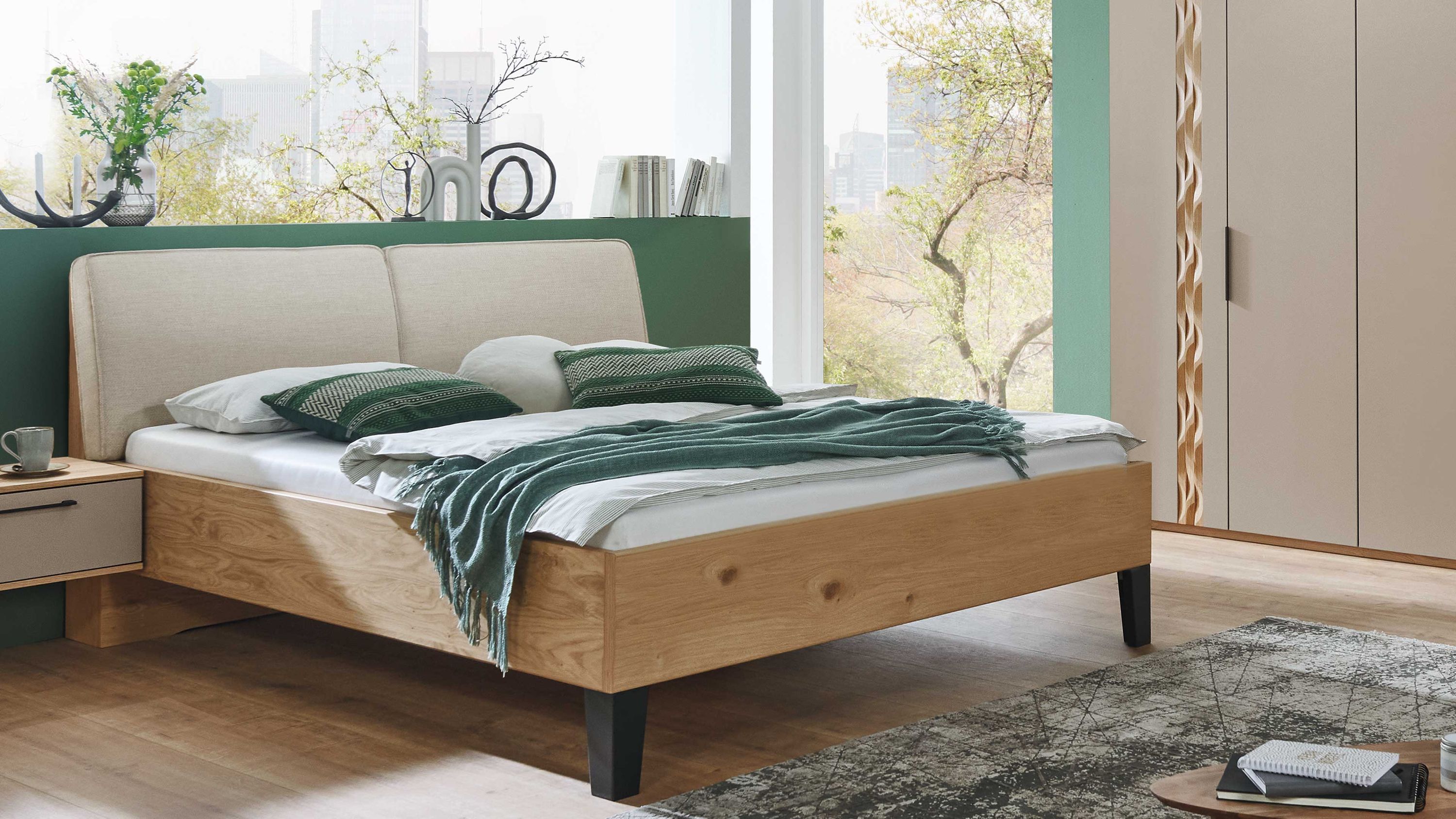 Bettgestell aus Holz mit beigem gepolstertem Kopfteil und schwarzen Füßen in einem Schlafzimmer