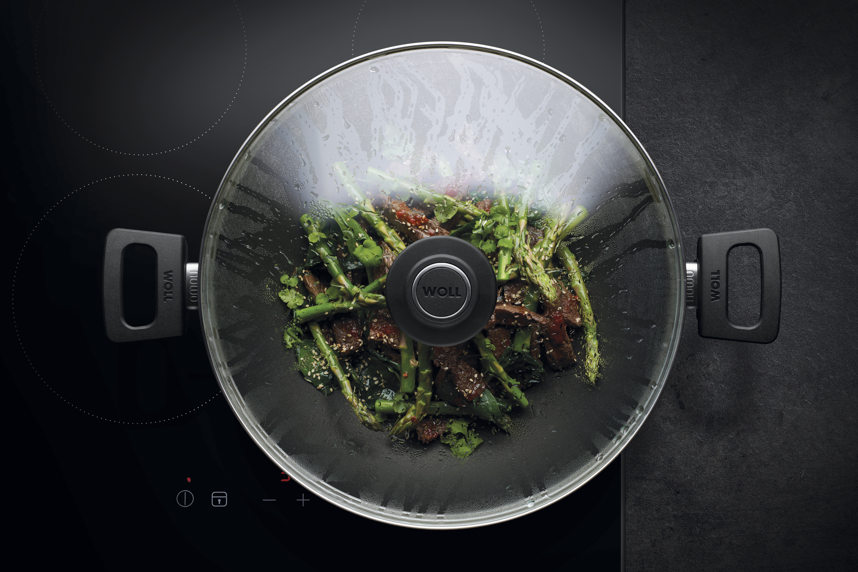 WOLL Wok mit Glasdeckel auf Herd, gefüllt mit grünem Gemüse und Fleisch.