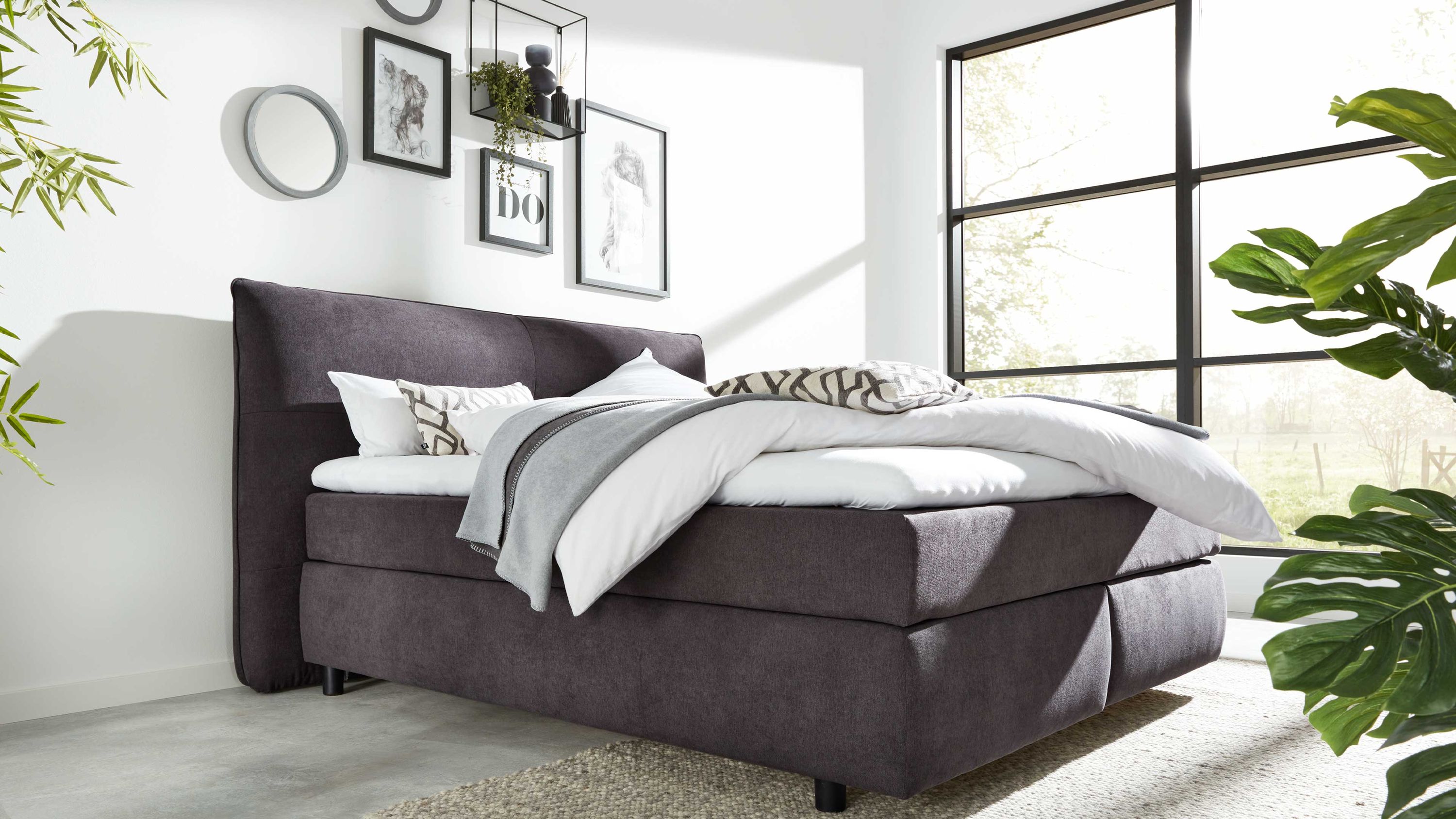 Boxspringbett mit dunkelgrauem Stoffbezug und gepolstertem Kopfteil in modernem Schlafzimmer